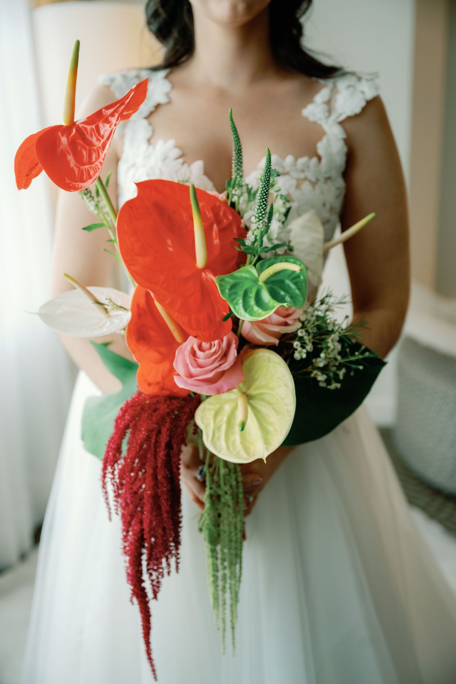 Elegant bridal bouquet featuring coral anthuriums, white roses, and cascading red amaranthus against a white dress.