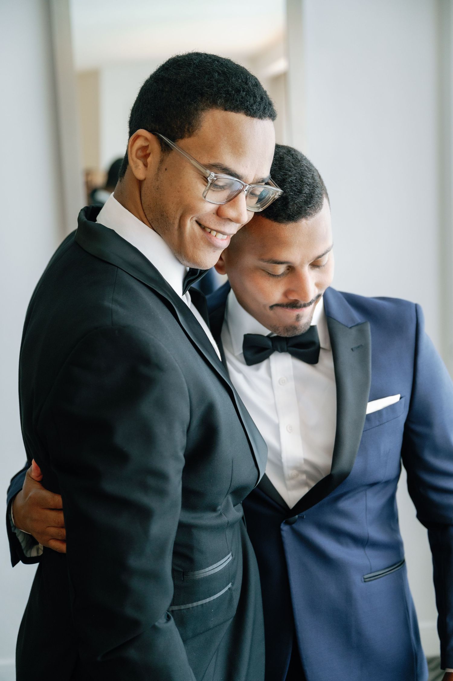 Two people in formal attire share an embrace while wearing black and navy suits at an elegant event.