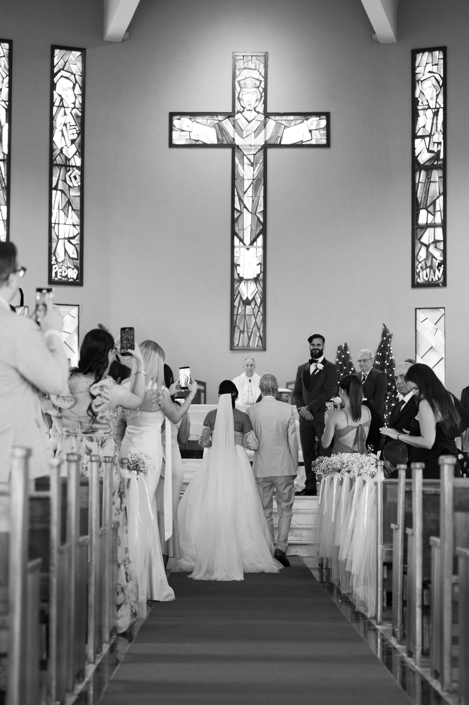 A black and white photo of a church wedding ceremony with stained glass windows and guests seated in wooden pews.