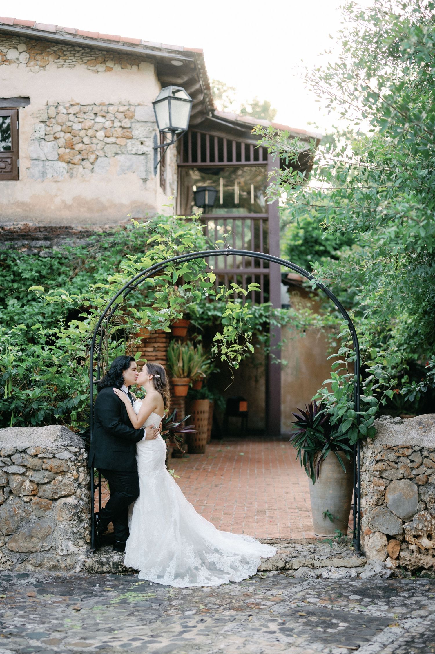 A couple shares intimate moments in a rustic stone courtyard with climbing vines and natural lighting.