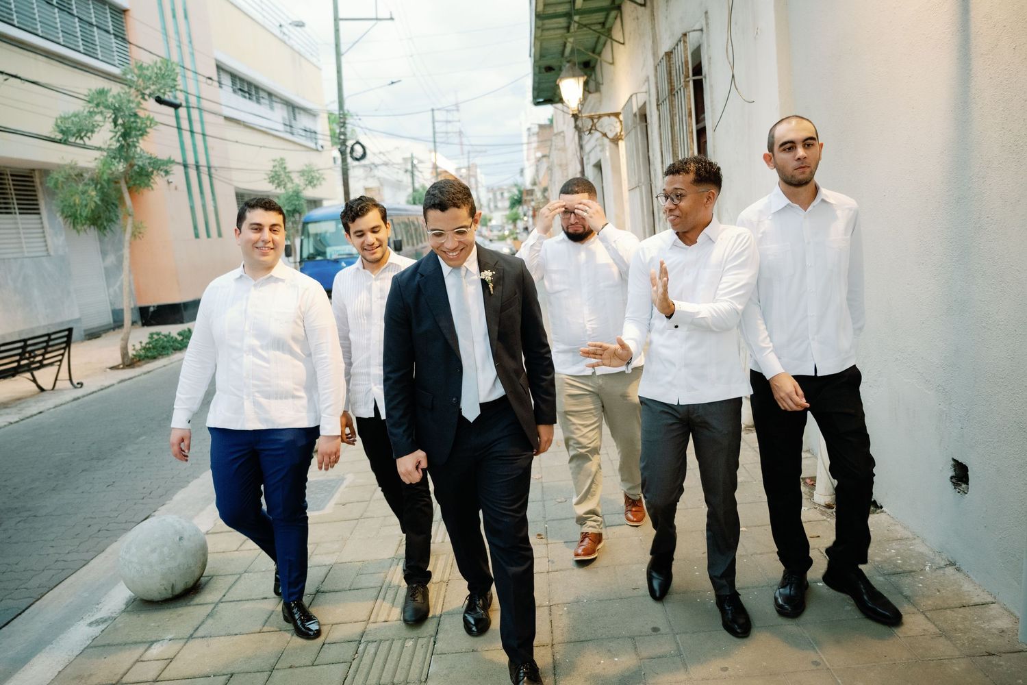 A group of people in white shirts and dark pants walk together down a street in a sequence of candid shots.