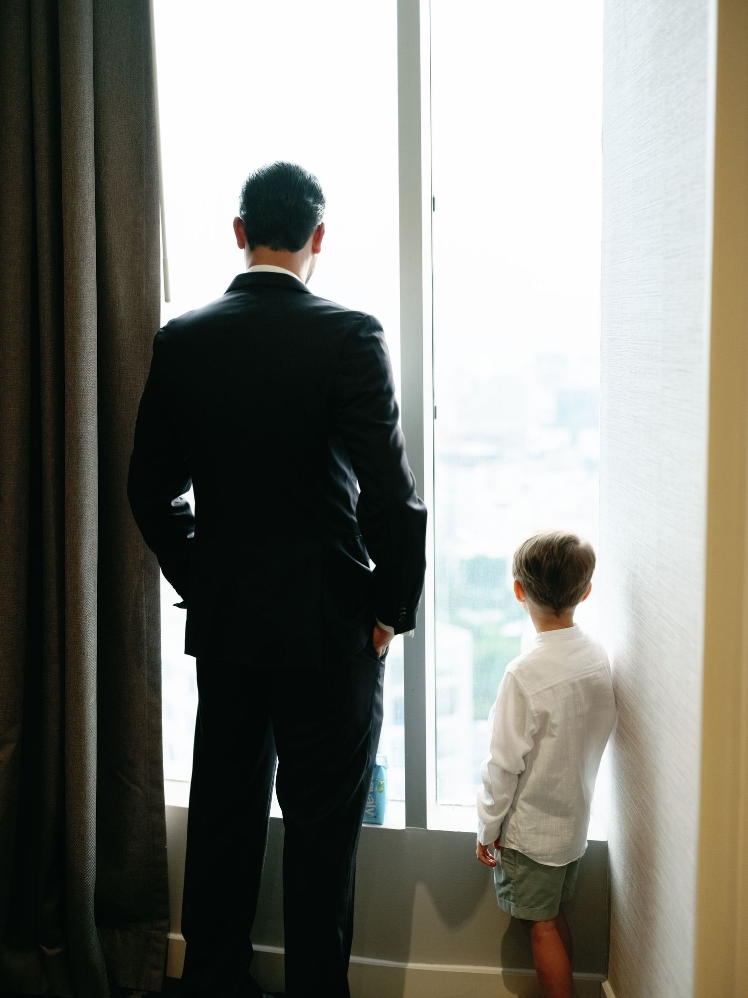 Business people in dark suits stand silhouetted against bright windows in an office building.
