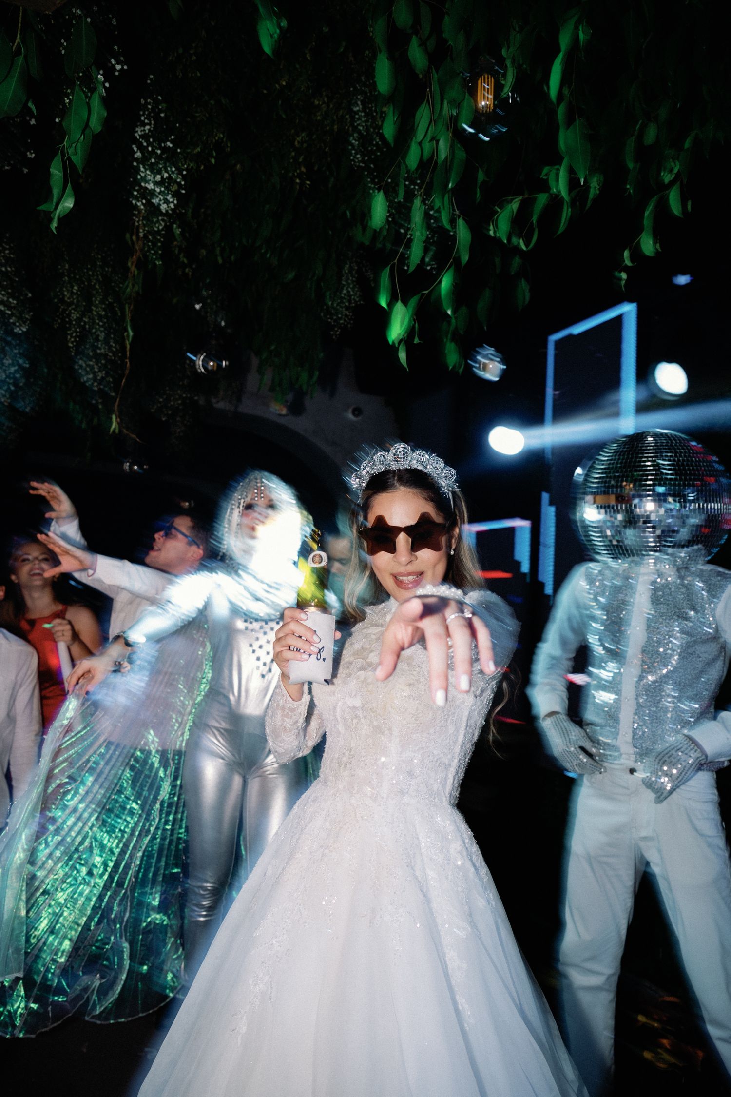 Wedding party members in white attire dancing under blue and green lighting effects.