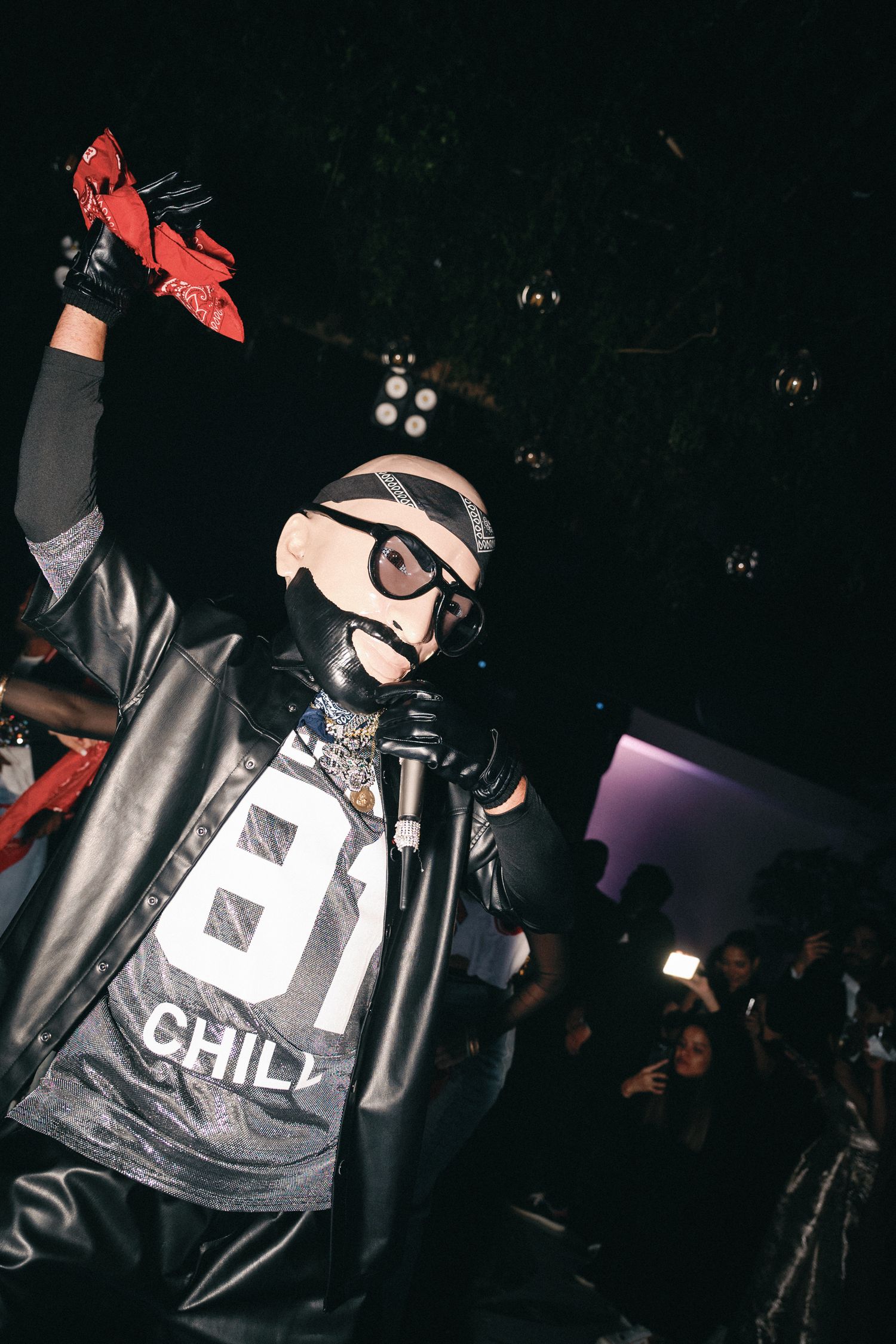 Person in metallic jacket and face mask performing under dramatic nightclub lighting.