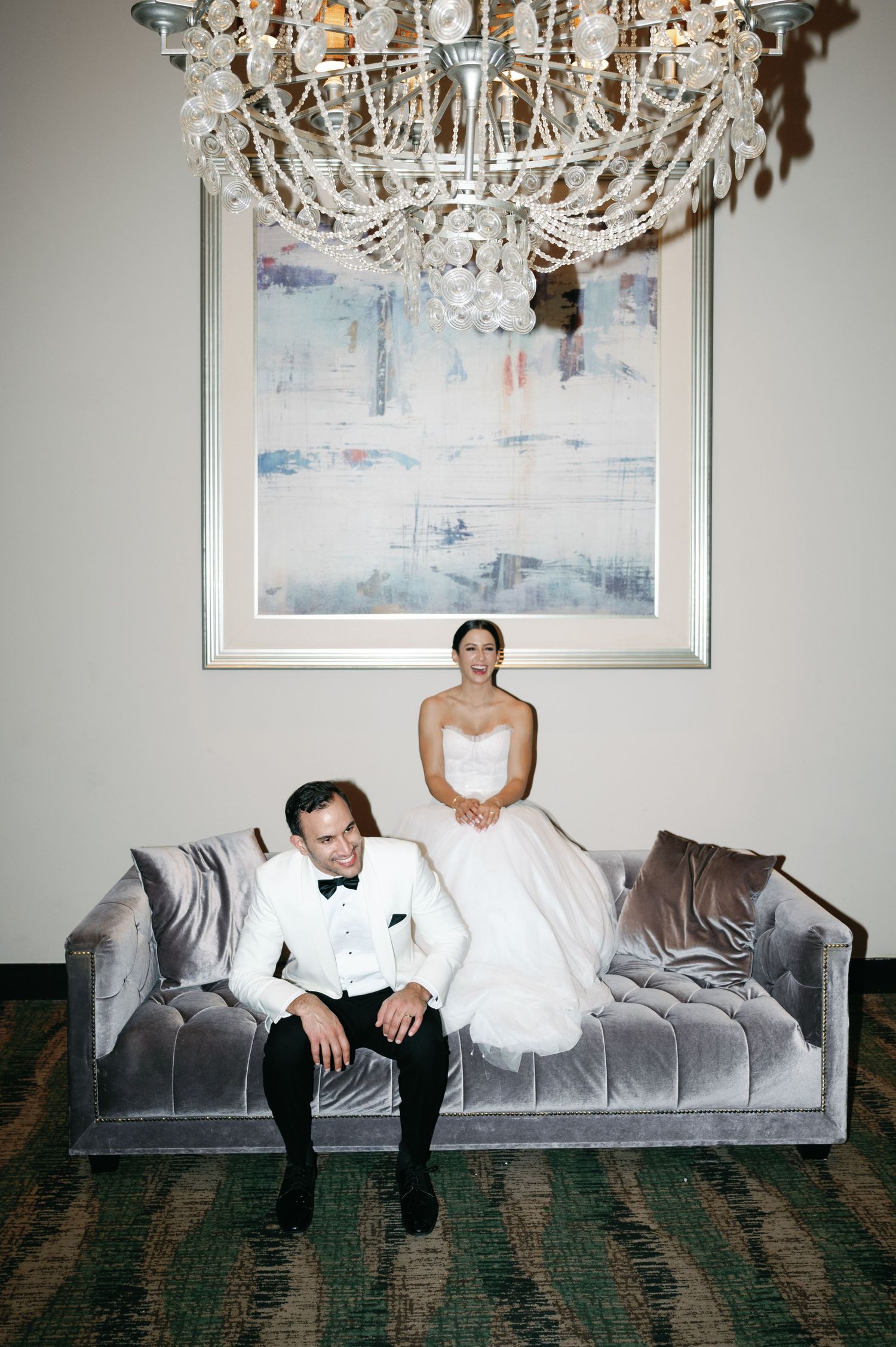 A series of five photos showing someone in formal attire sitting on a gray couch beneath a crystal chandelier and artwork.