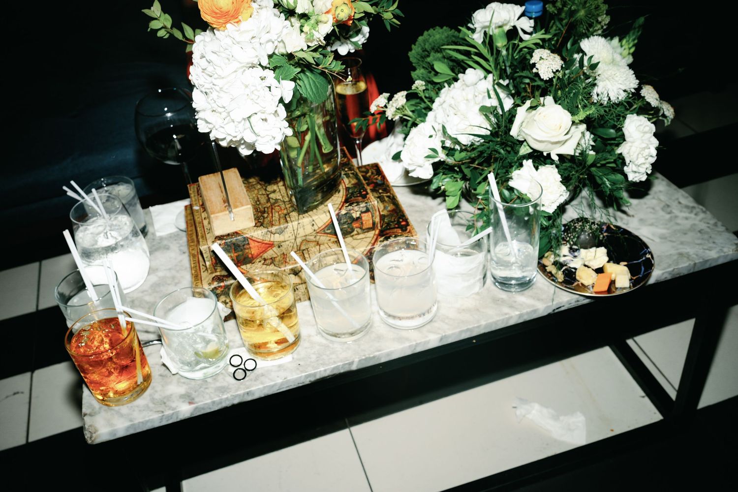 Wedding reception table settings with white floral centerpieces and decorative elements arranged on a dark surface.