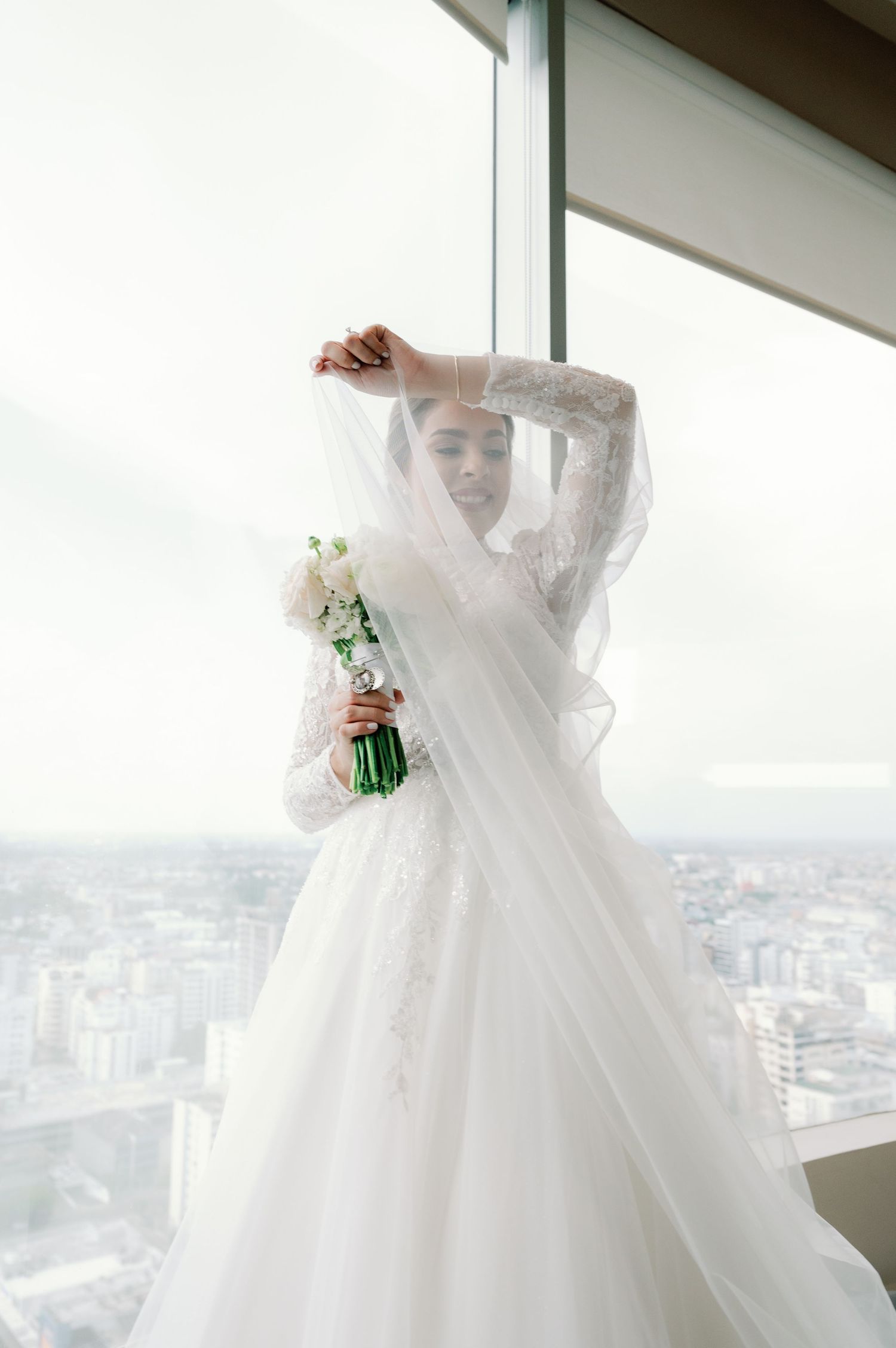 A white wedding dress with long lace sleeves and full tulle skirt is displayed in a series of shots near a window.