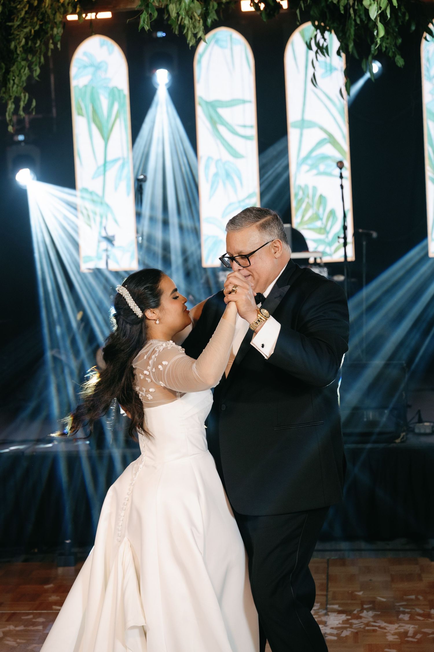 A couple shares a dance at their wedding reception with stained glass windows and dramatic lighting beams in the background.