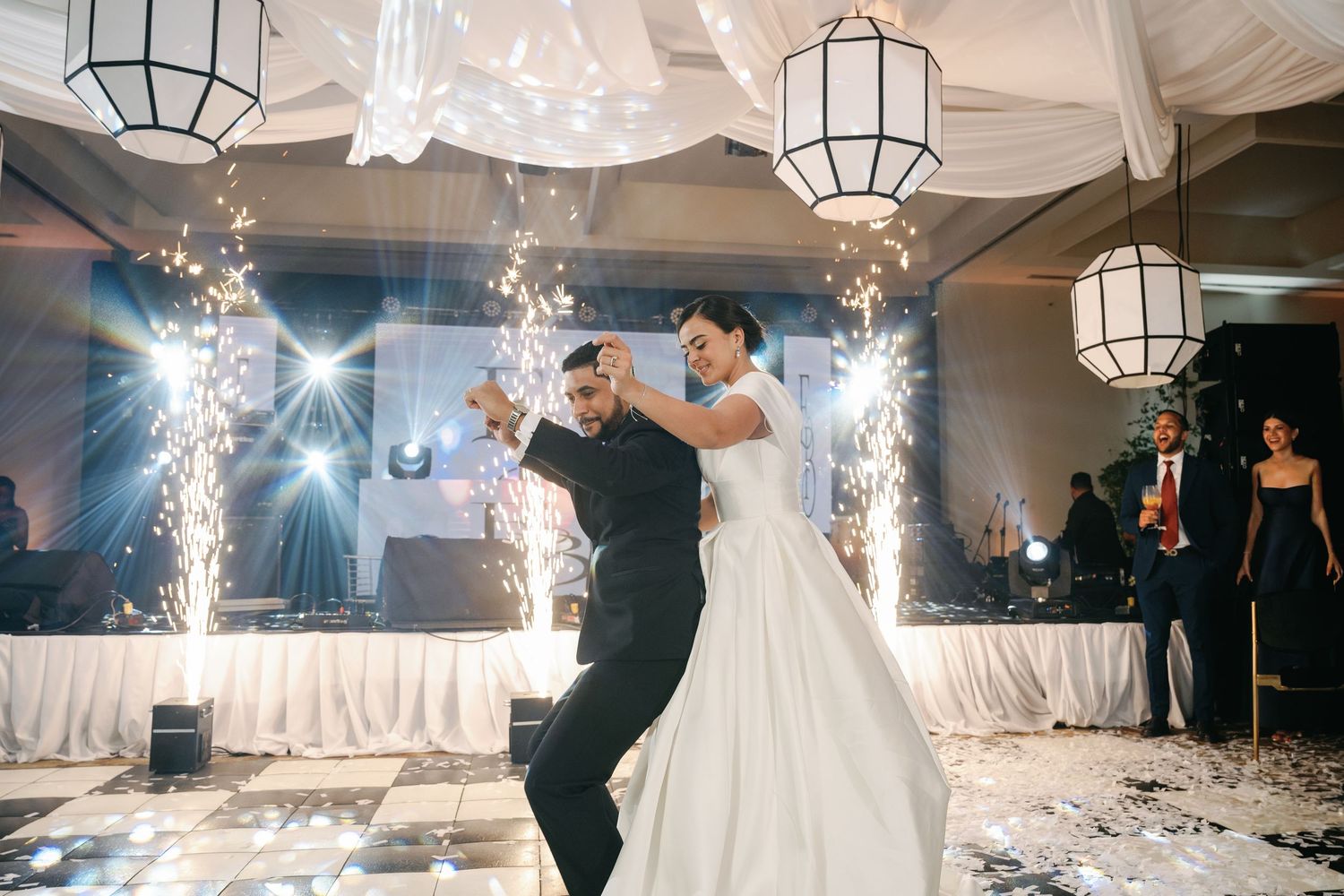 Newlyweds dance together on a white dance floor with sparklers and lanterns creating a magical atmosphere at their reception.