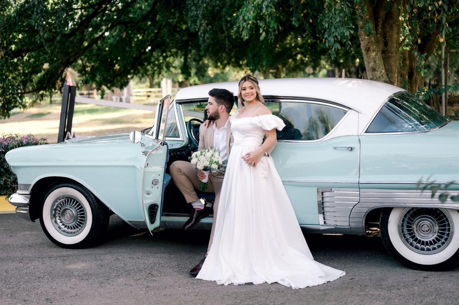 Vintage blue Cadillac with white-wall tires parked on tree-lined street creates romantic wedding scene.