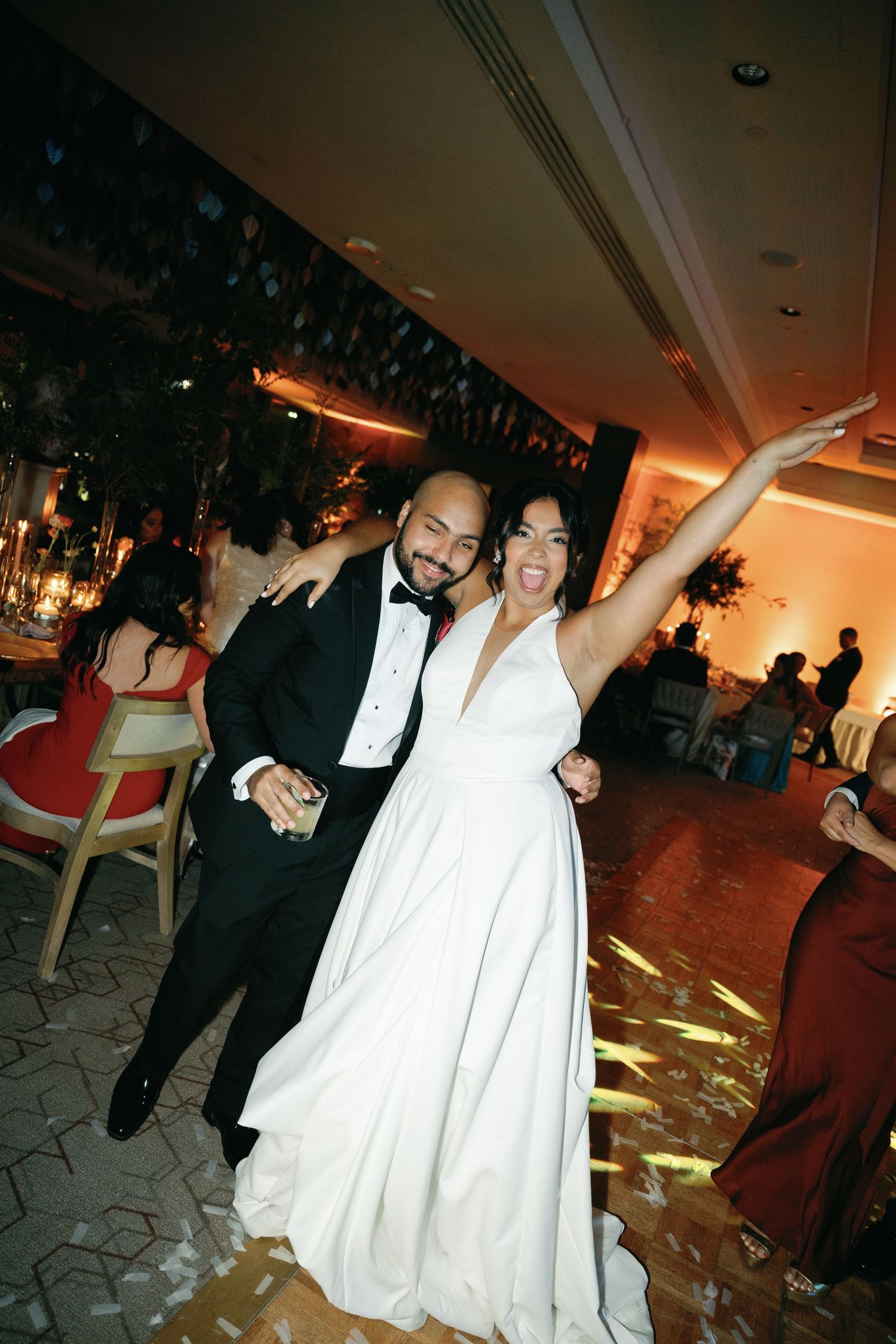 Wedding reception guests dance and celebrate on a dimly lit dance floor decorated with ambient lighting.