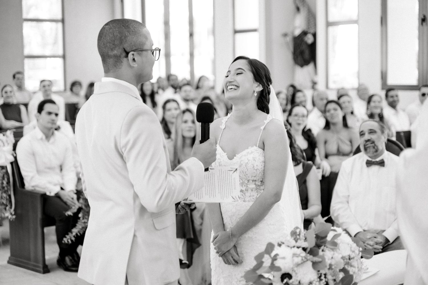 A joyful moment captured in black and white as a bride and groom share a laugh during their wedding ceremony in a church.