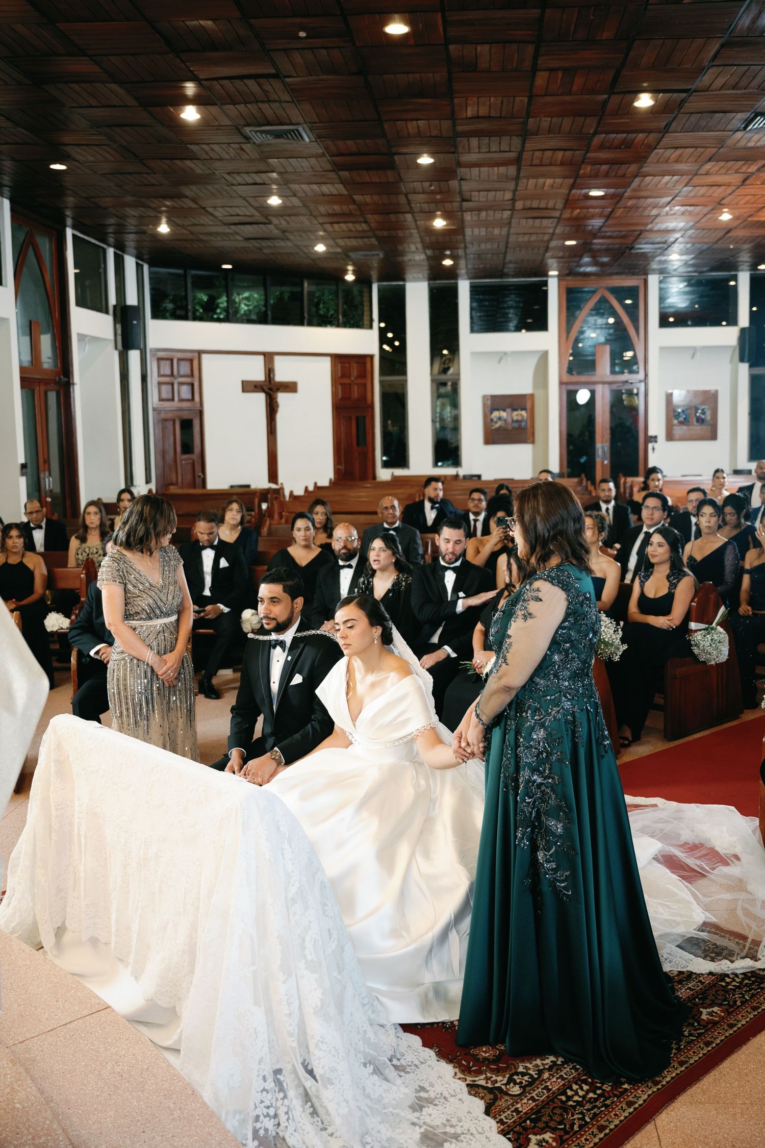 Wedding guests watch as a bride shows off her flowing white dress train in a church ceremony.