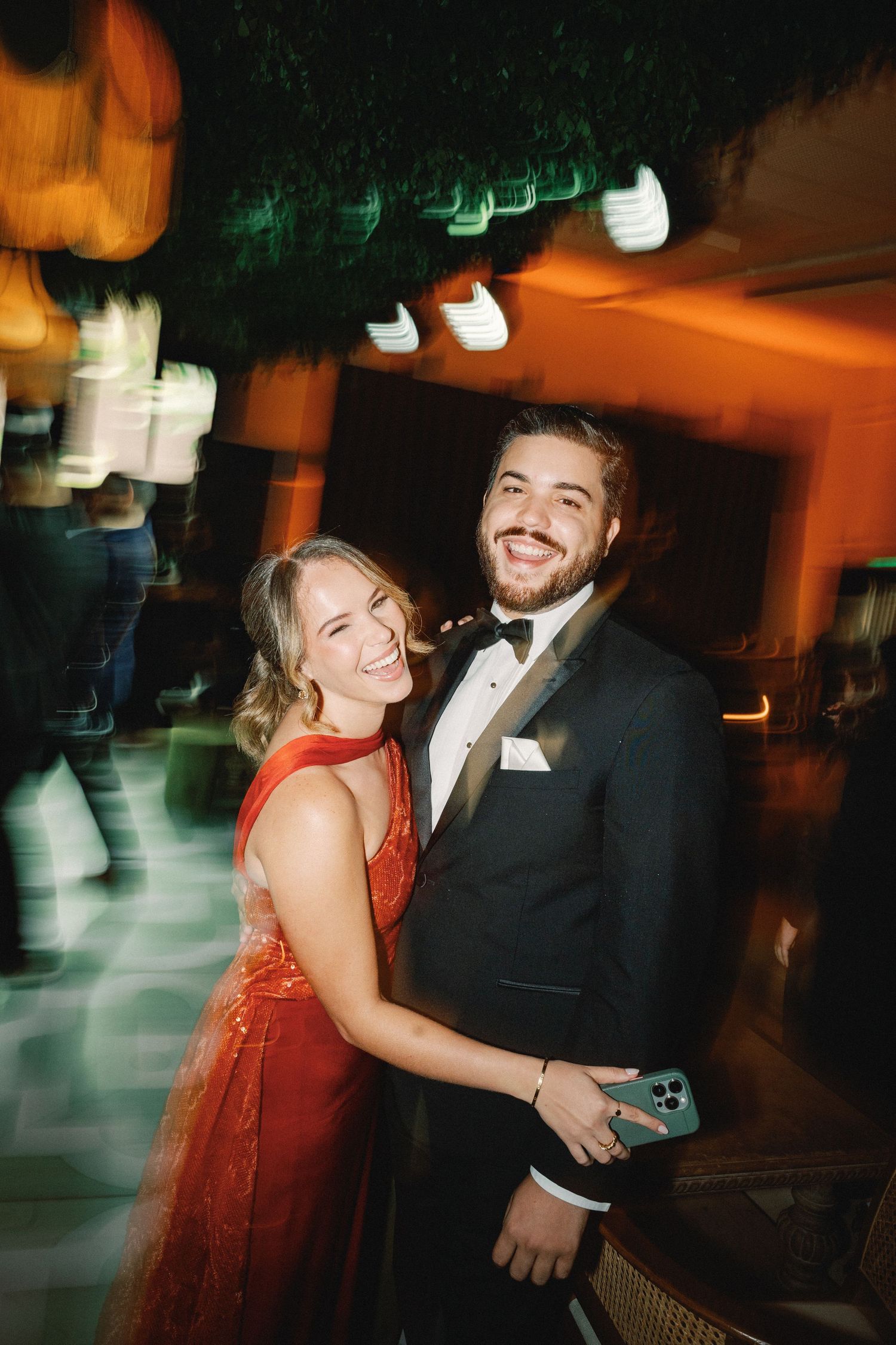 A couple dancing together at an evening event, with the woman wearing a red dress and the man in a black suit.