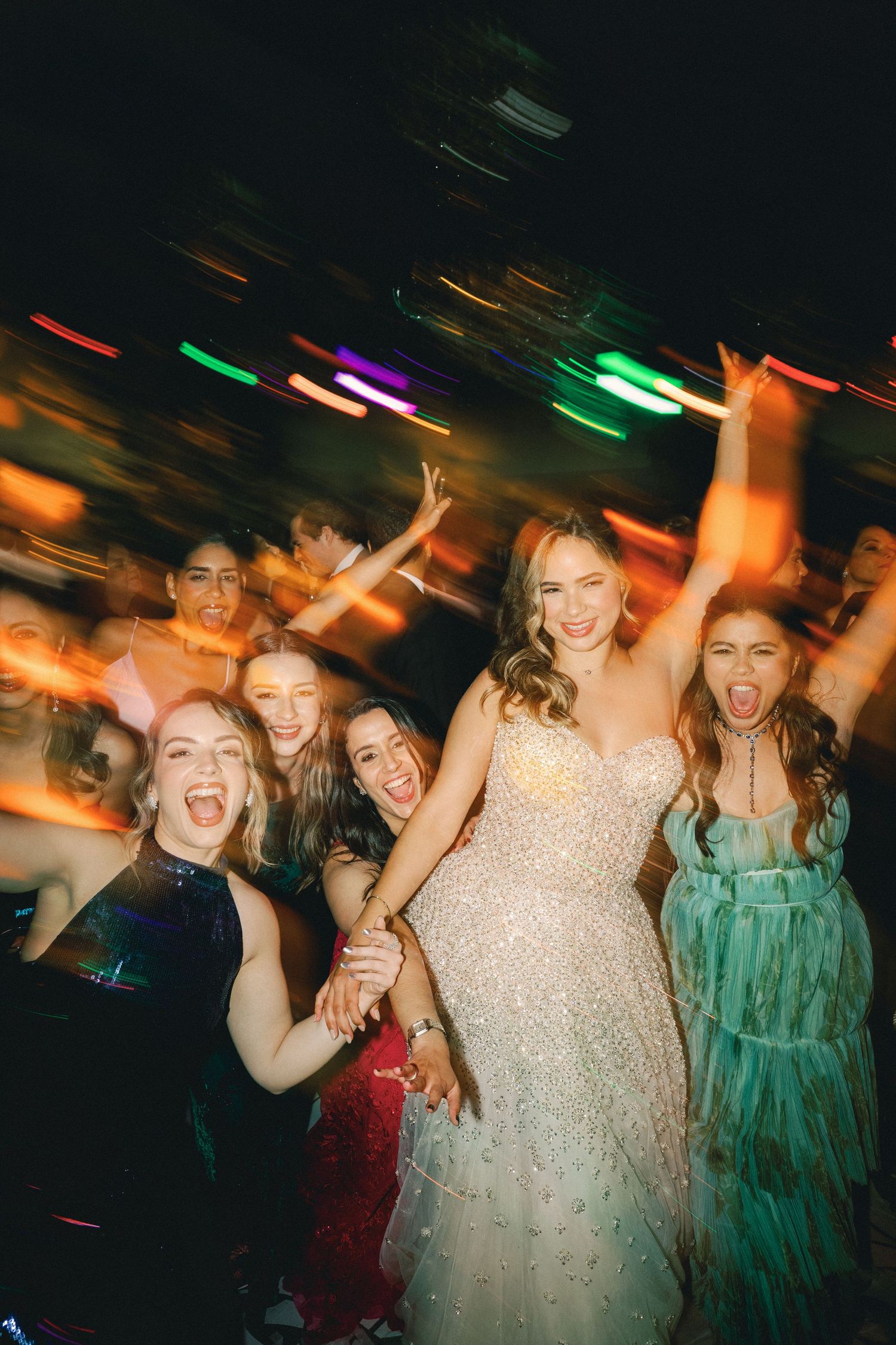 Group of party guests dancing and celebrating under colorful disco lights at a nighttime event.