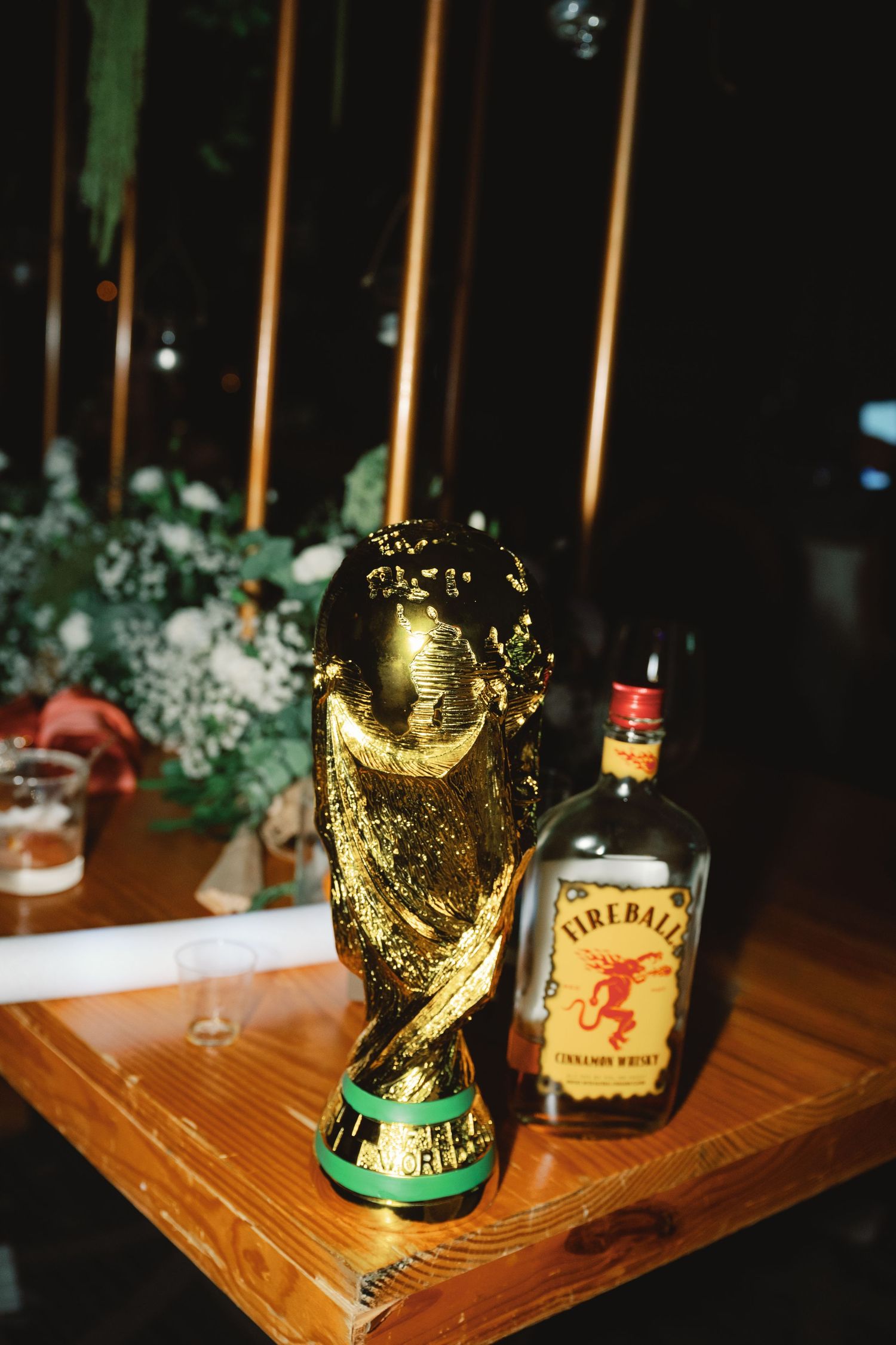 A golden FIFA World Cup trophy displayed next to a bottle of Fireball whiskey on a wooden surface.