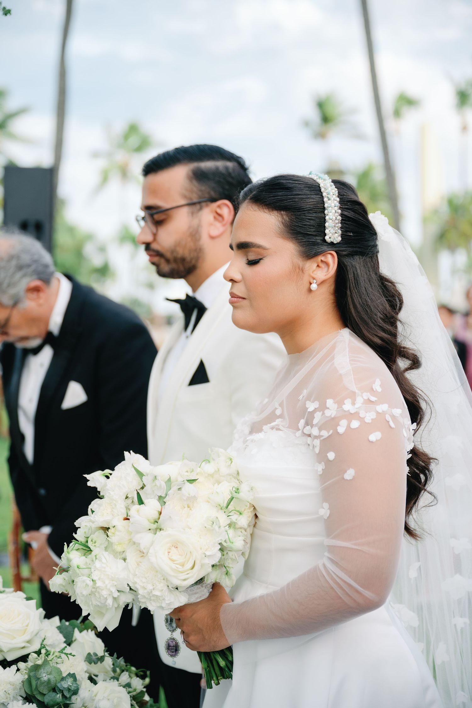 Elegant outdoor wedding ceremony with white floral bouquets and sheer lace details.