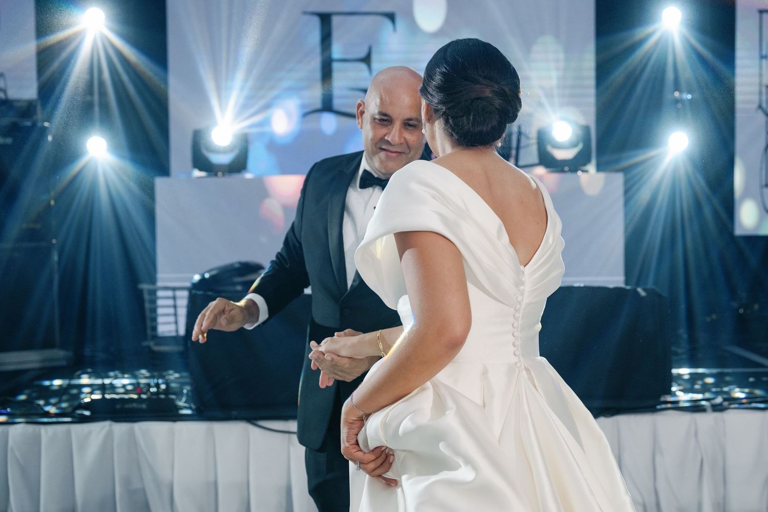 Couples dance together at an elegant wedding reception with dramatic lighting and lens flares creating a romantic atmosphere.