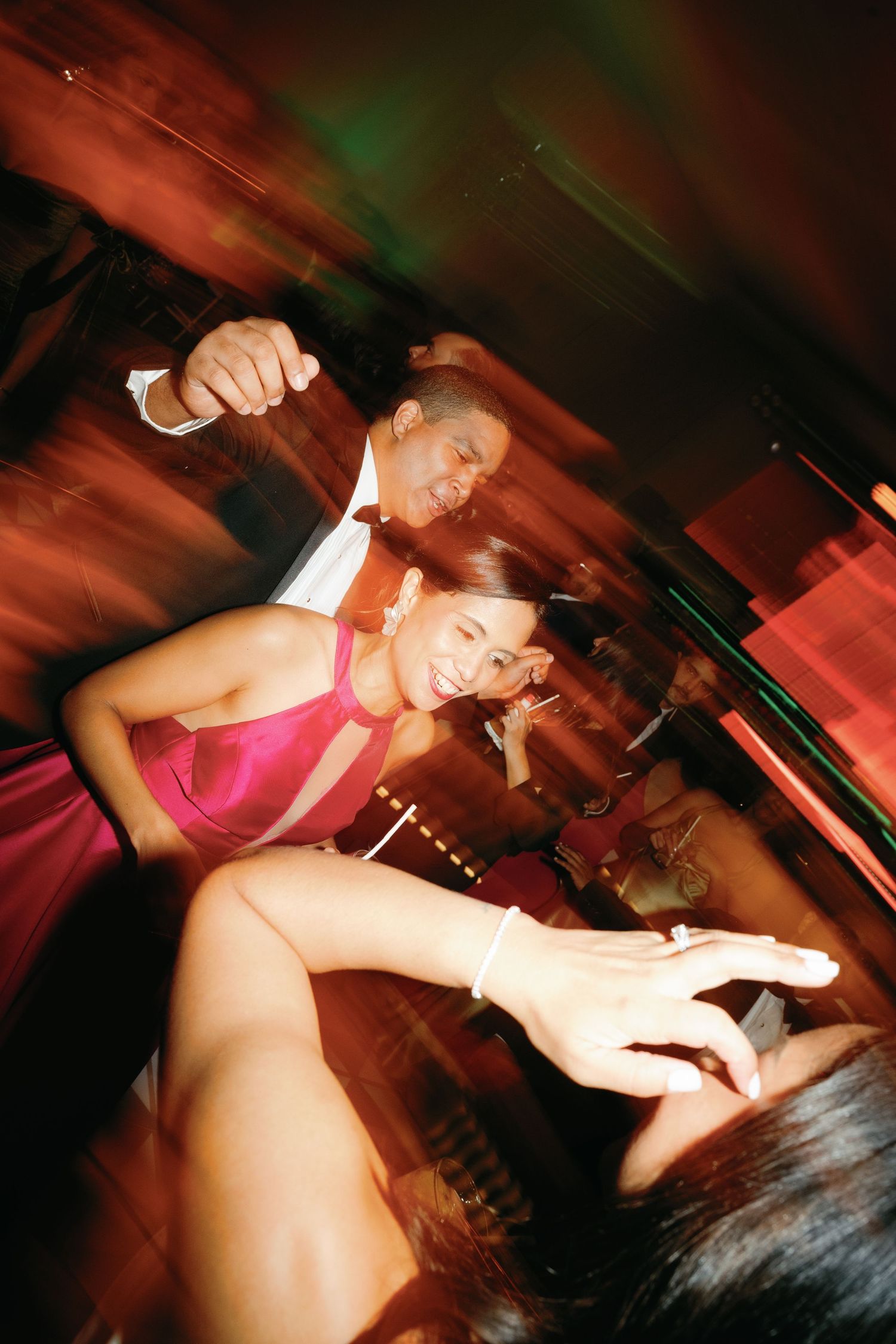 Dancers in pink costumes perform dynamic movements under dramatic red stage lighting at a nightclub.