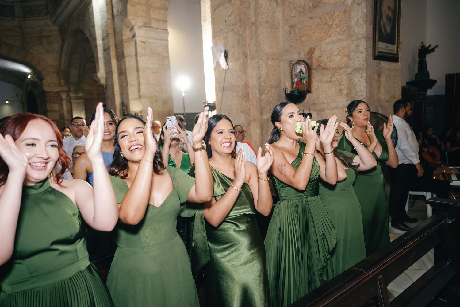 Wedding party in green dresses celebrating with animated expressions in a church setting.