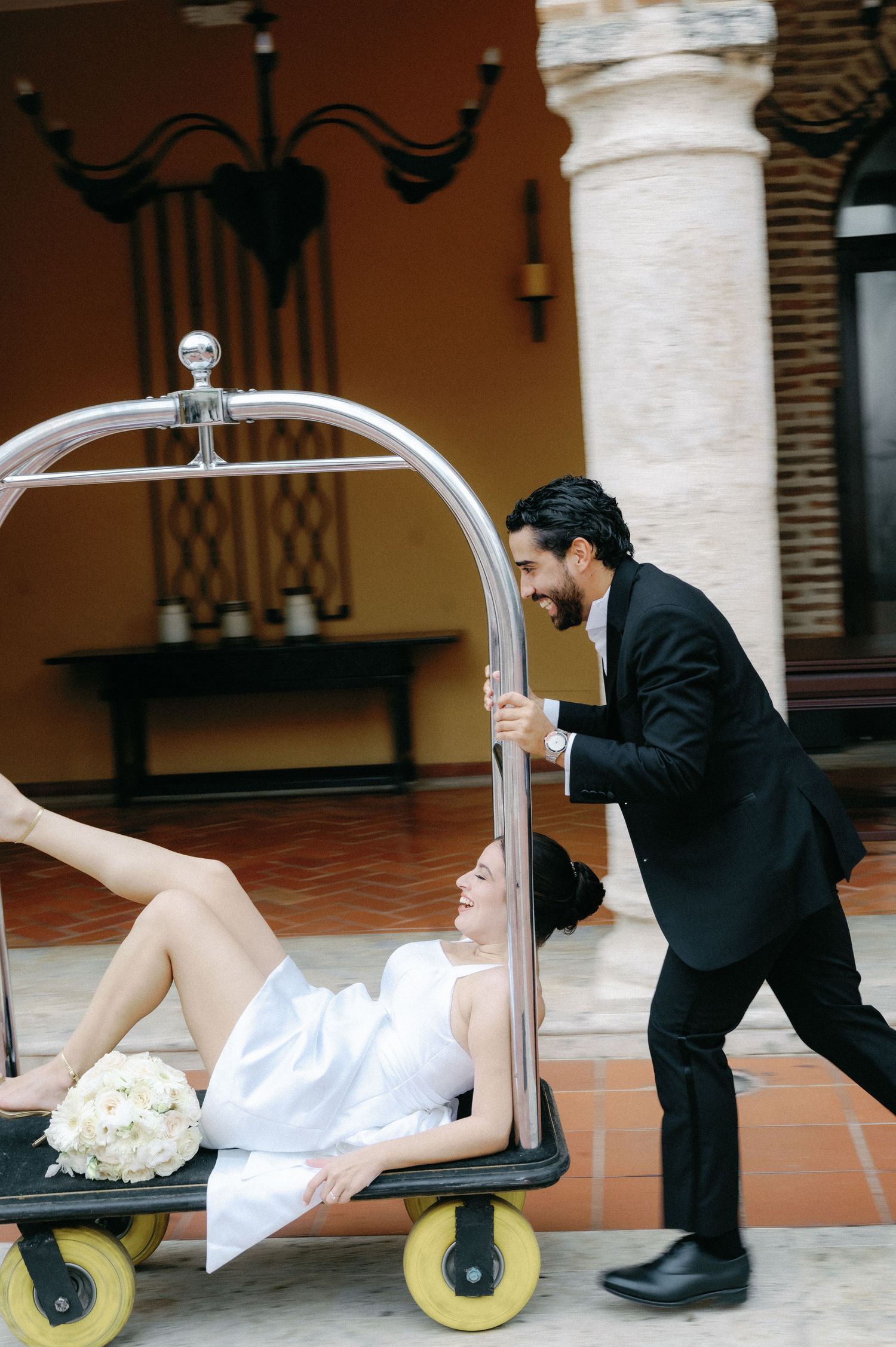 A creative wedding photo sequence showing a bride being playfully pushed on a luggage cart by a groom in formal attire.