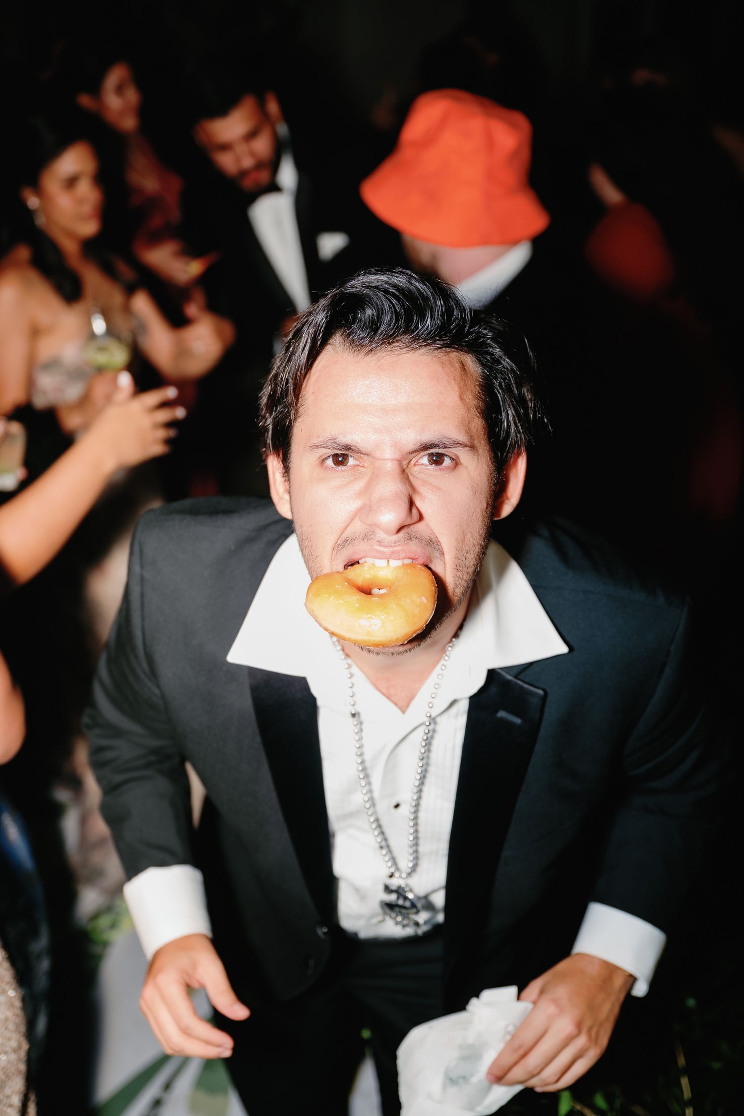 Person in formal attire taking a bite of a hamburger at what appears to be an elegant event or party.