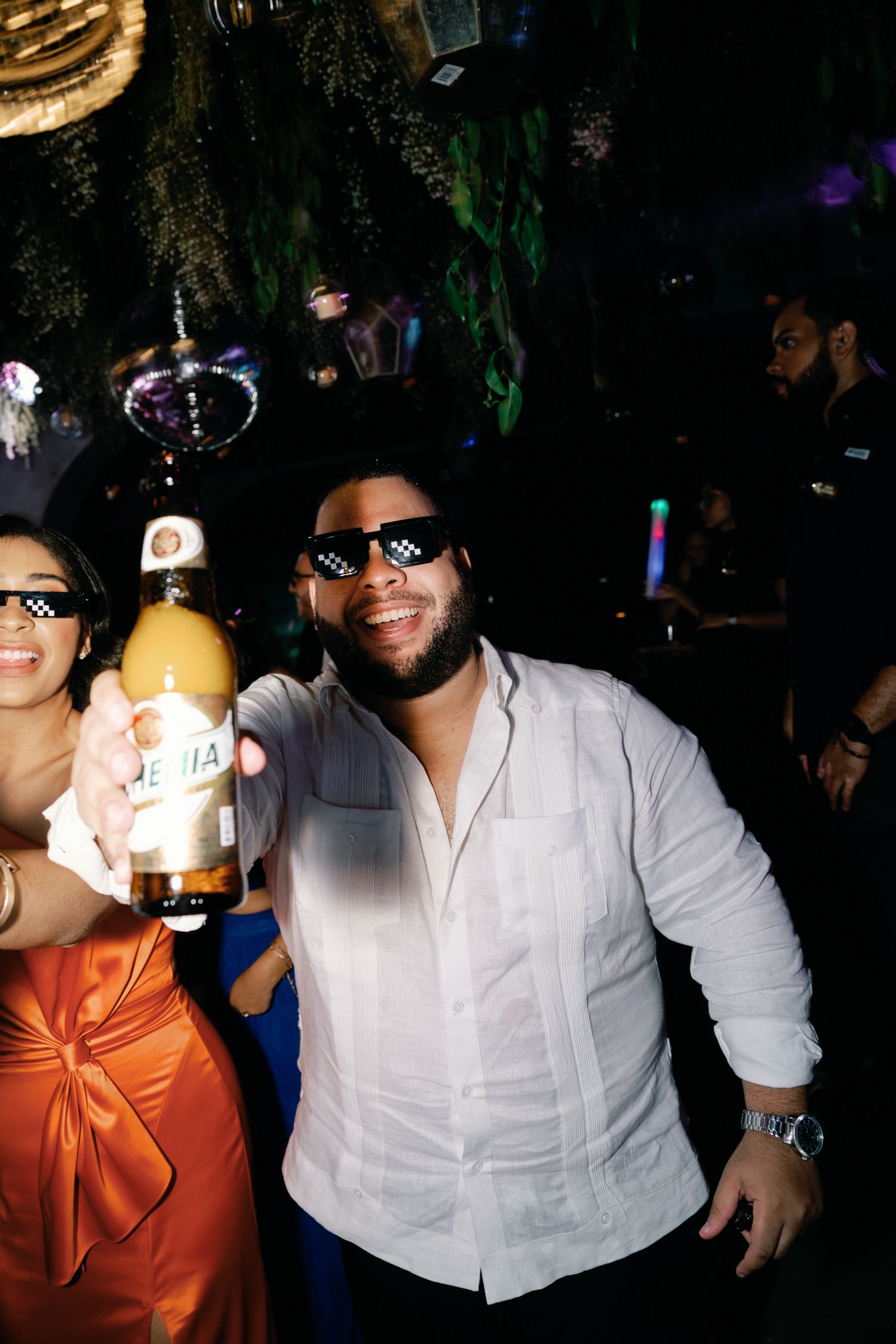 Partygoers enjoying a nightclub atmosphere with people in white shirts and orange attire dancing under dark lighting.