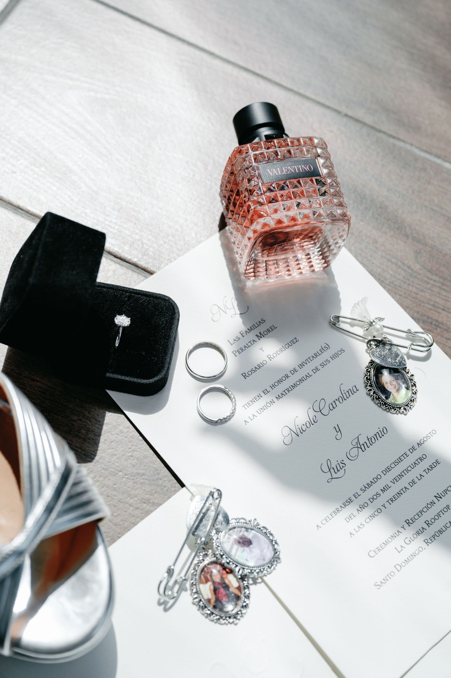 Wedding rings and invitation displayed on a light gray surface with black ring boxes and pink decor accents.