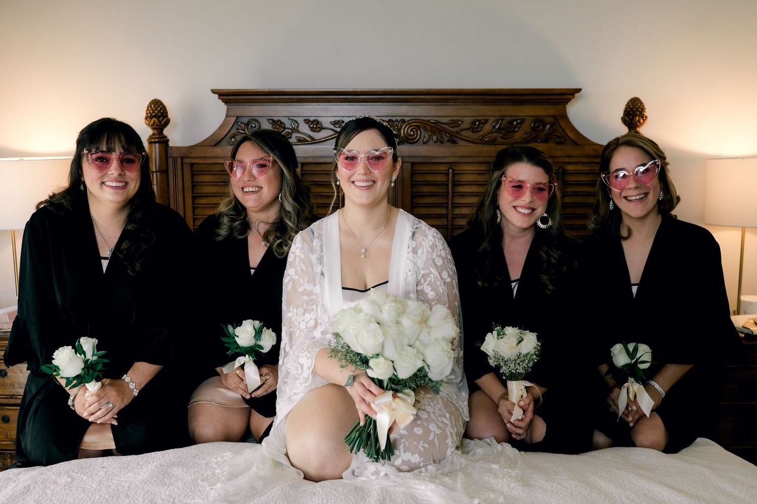 A group of people in formal attire holding white floral bouquets stand together for a wedding party photo.
