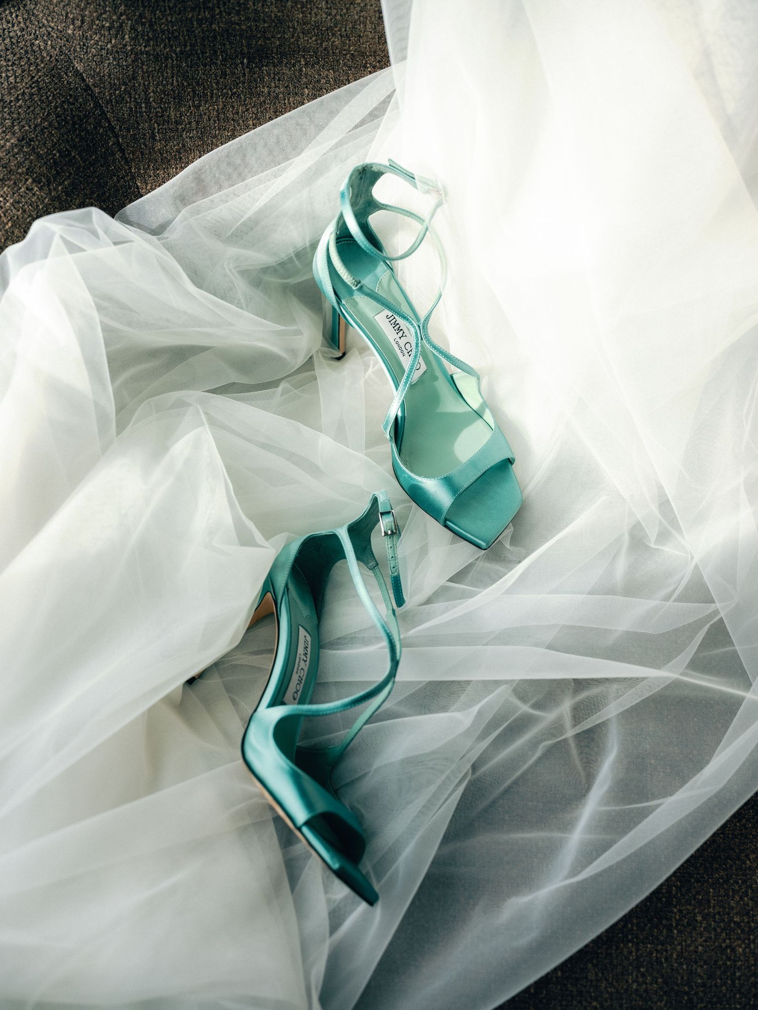 A pair of mint green strappy high heel sandals resting on flowing white tulle fabric.