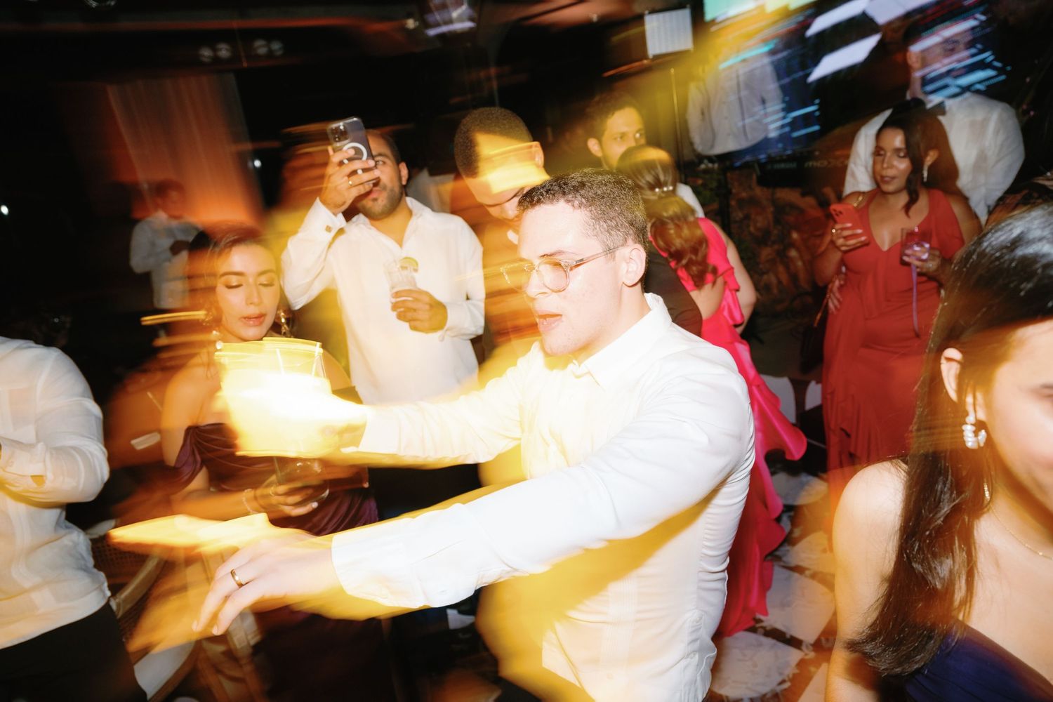People dancing and celebrating at a lively party with warm lighting and festive atmosphere.