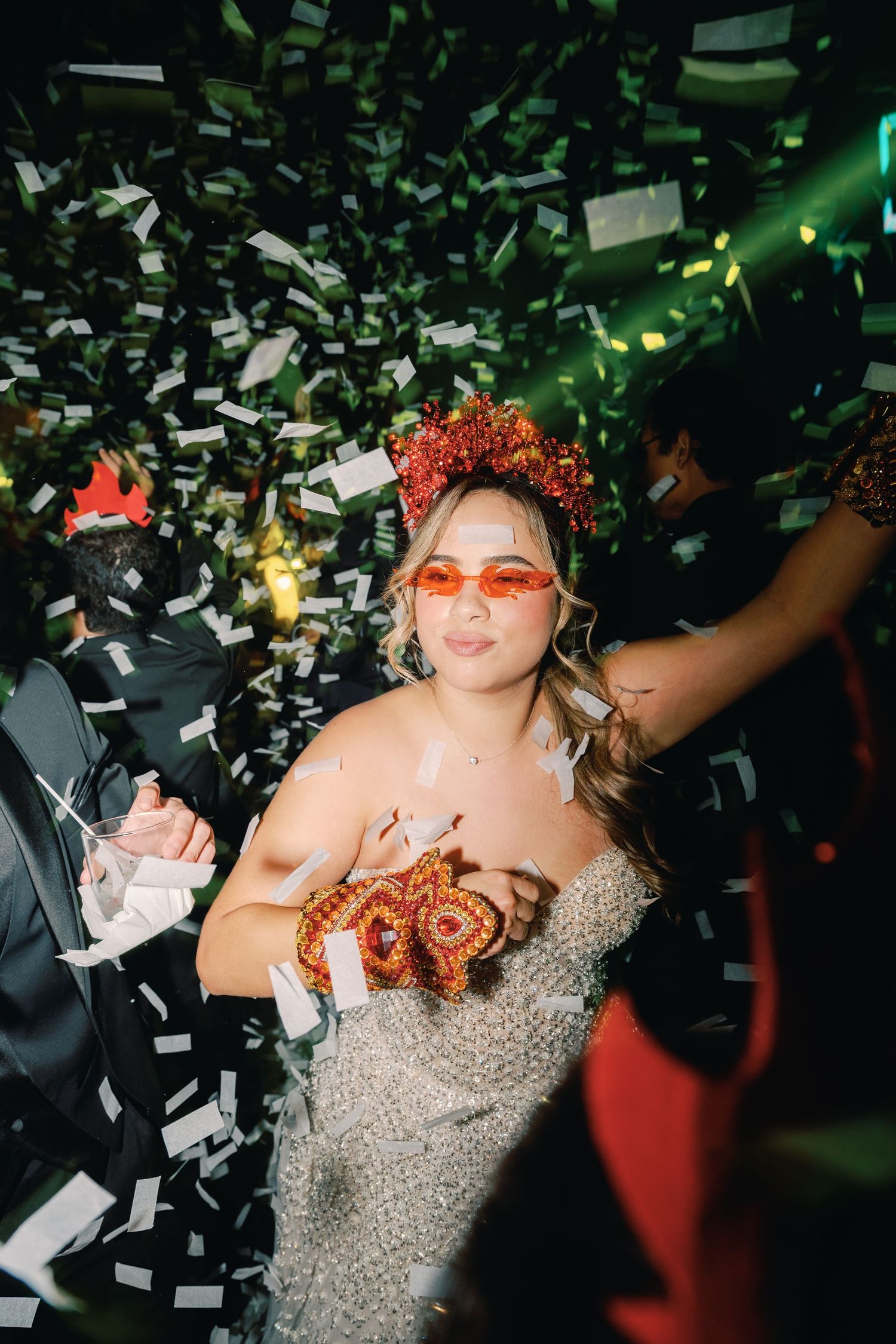 Dancing partygoers celebrate with confetti falling under green lighting at a festive event.