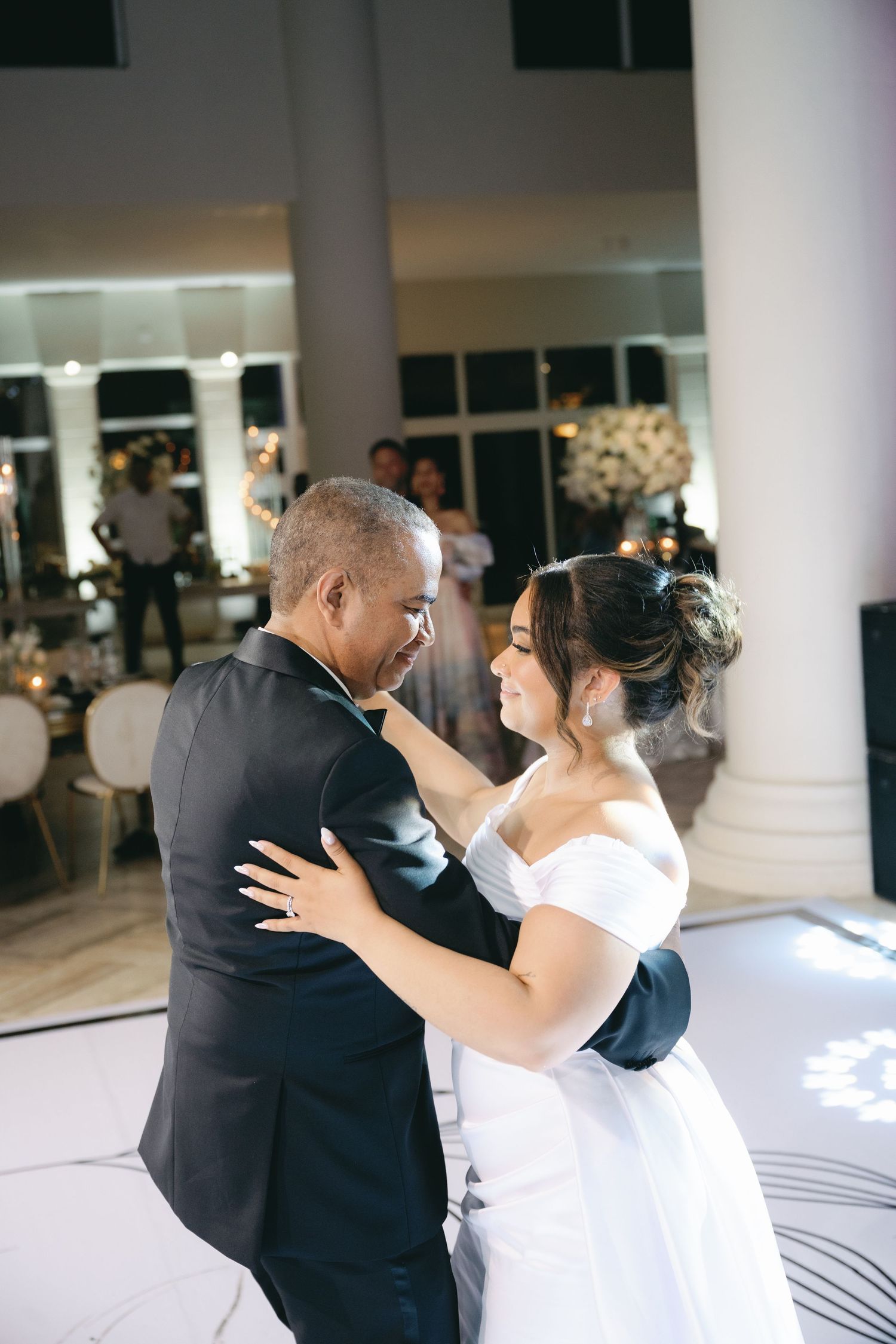 A tender moment during a wedding dance in a white decorated reception hall with columns and mirrors.