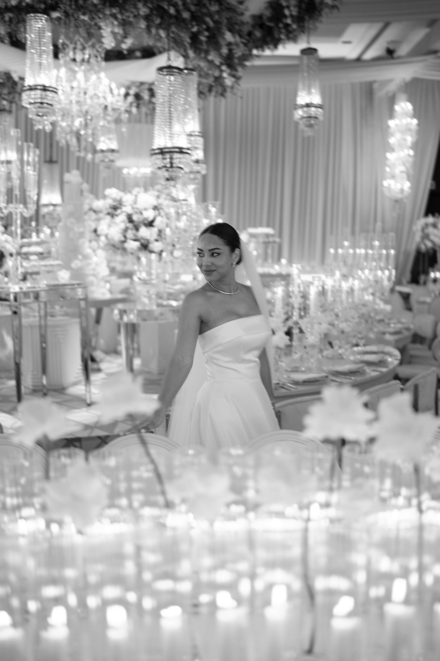 An elegant white wedding reception venue features crystal chandeliers and floral centerpieces creating a luxurious atmosphere.
