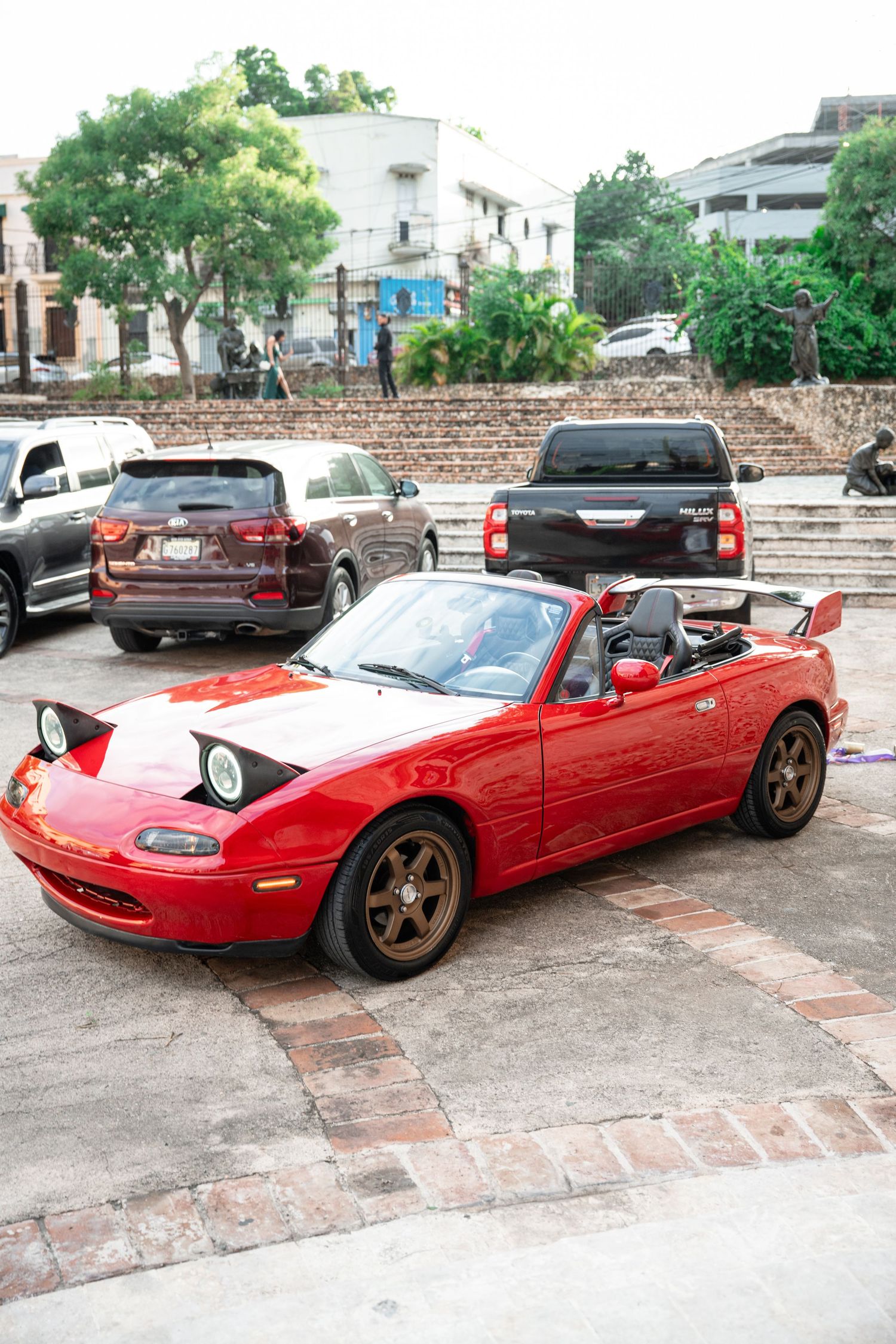 A red Mazda Miata convertible sports car shown from multiple angles parked on a brick driveway with bronze wheels.