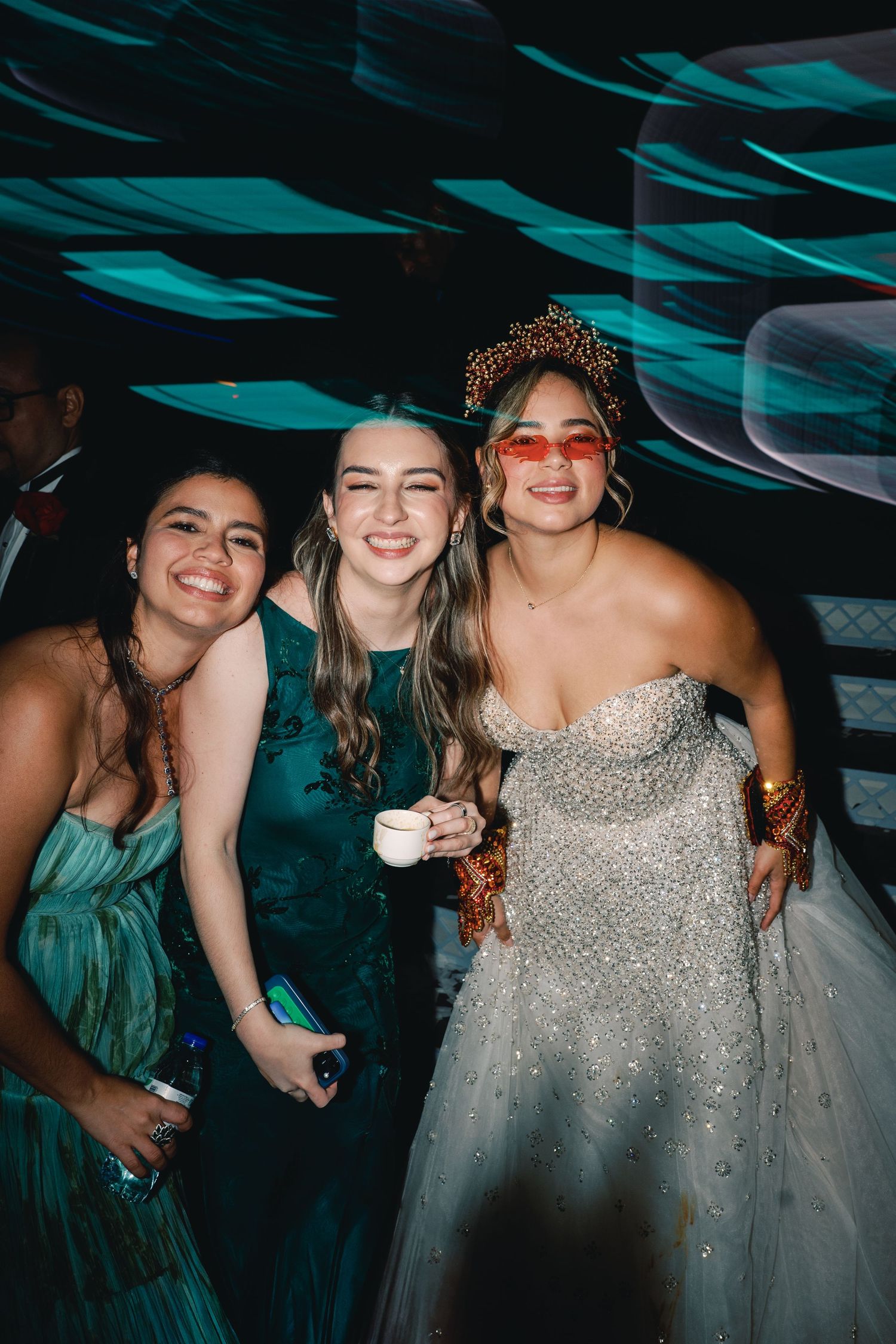 A group of friends in formal attire pose together under blue lighting at an elegant evening celebration.