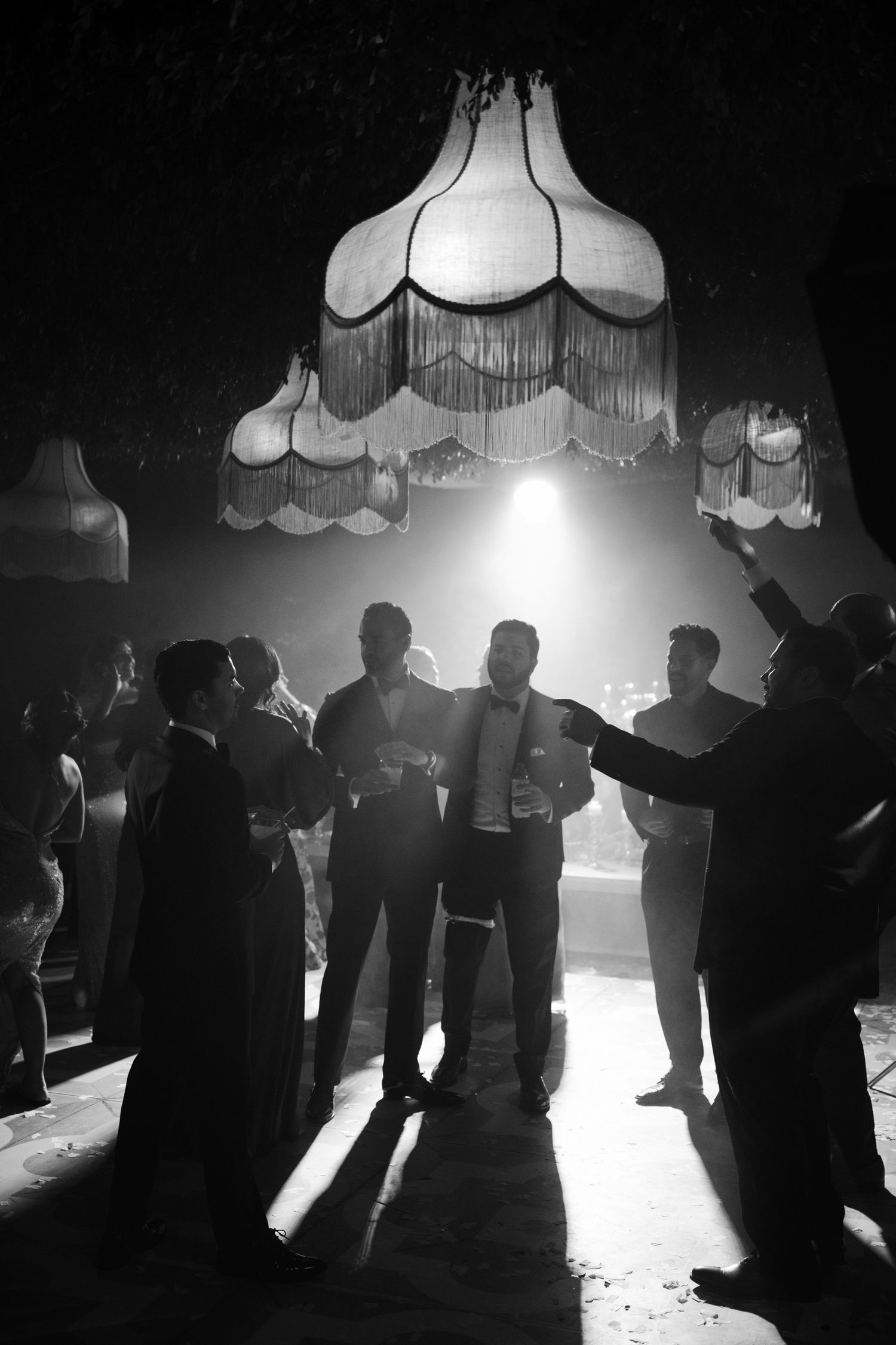 Silhouettes of dancers in a dimly lit nightclub with dramatic overhead lighting creating atmospheric shadows.