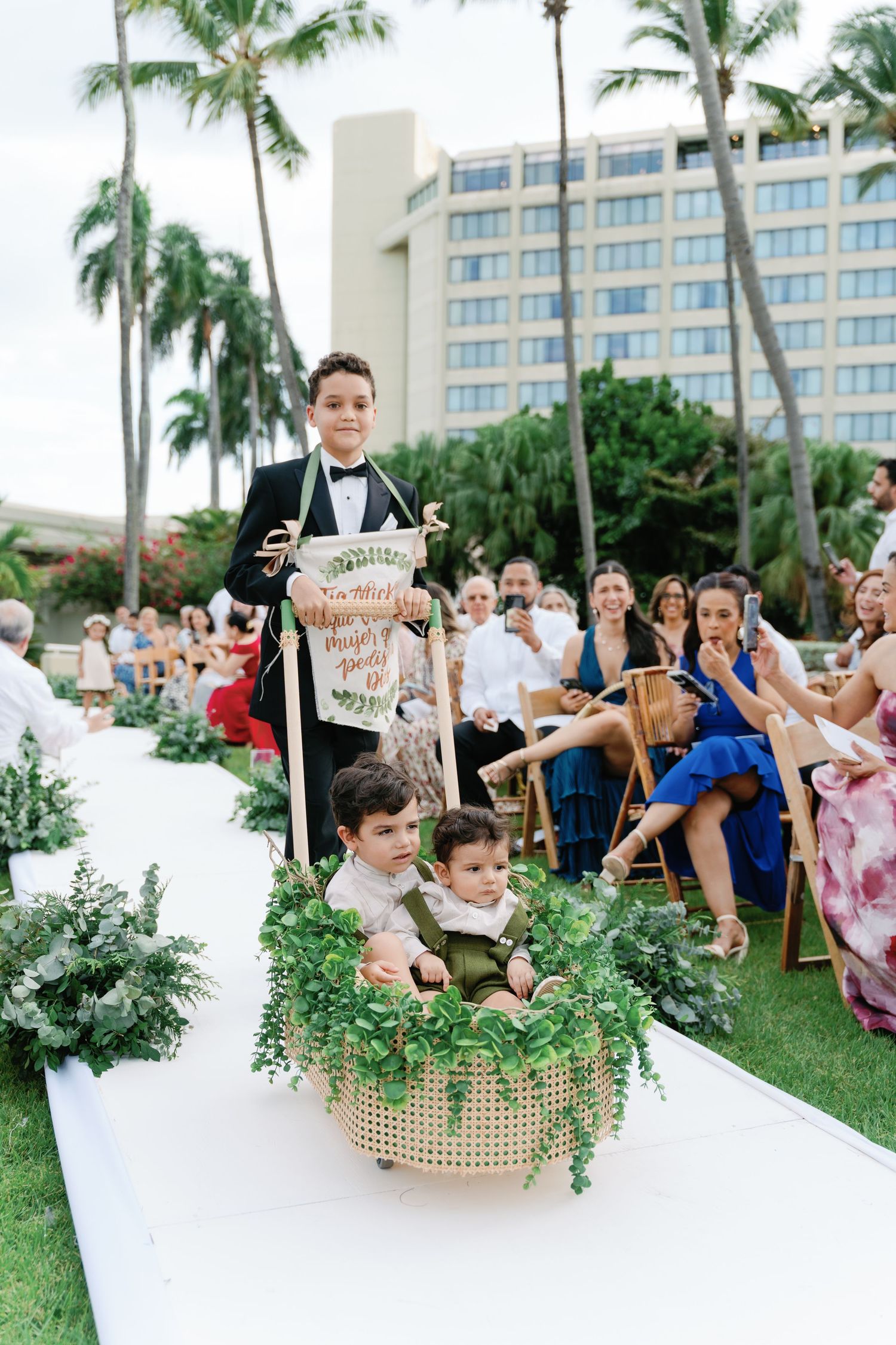 Wedding ceremony setup with white aisle runner and greenery decorations at a tropical resort.