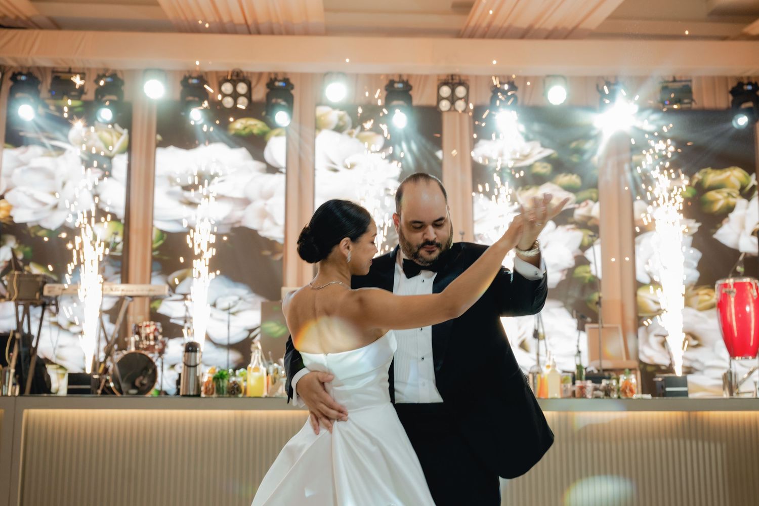 Newlywed couple shares their first dance on a wooden dance floor under warm lighting at an elegant indoor reception.