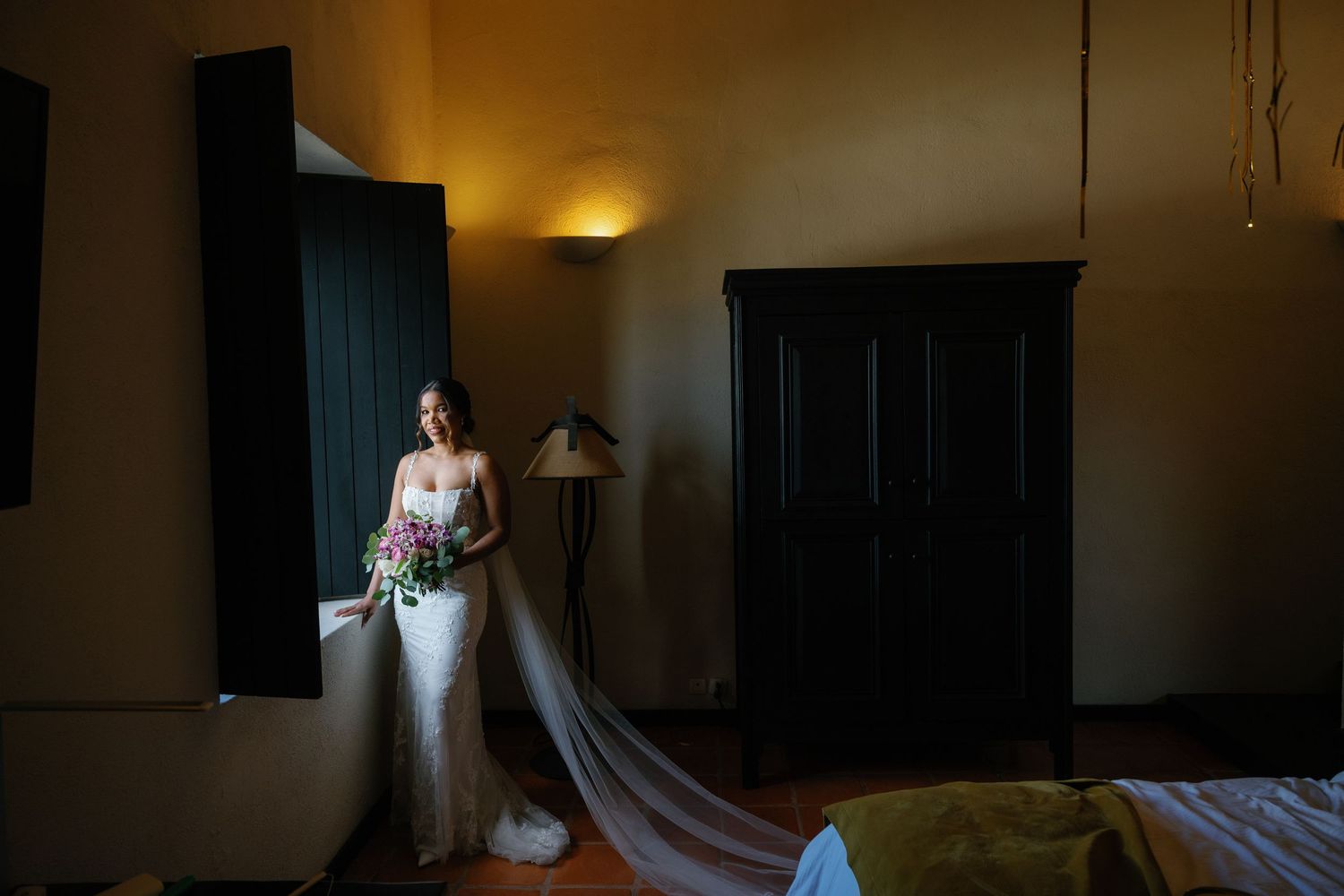 A bride in a white wedding dress stands in a dimly lit room with warm ambient lighting.