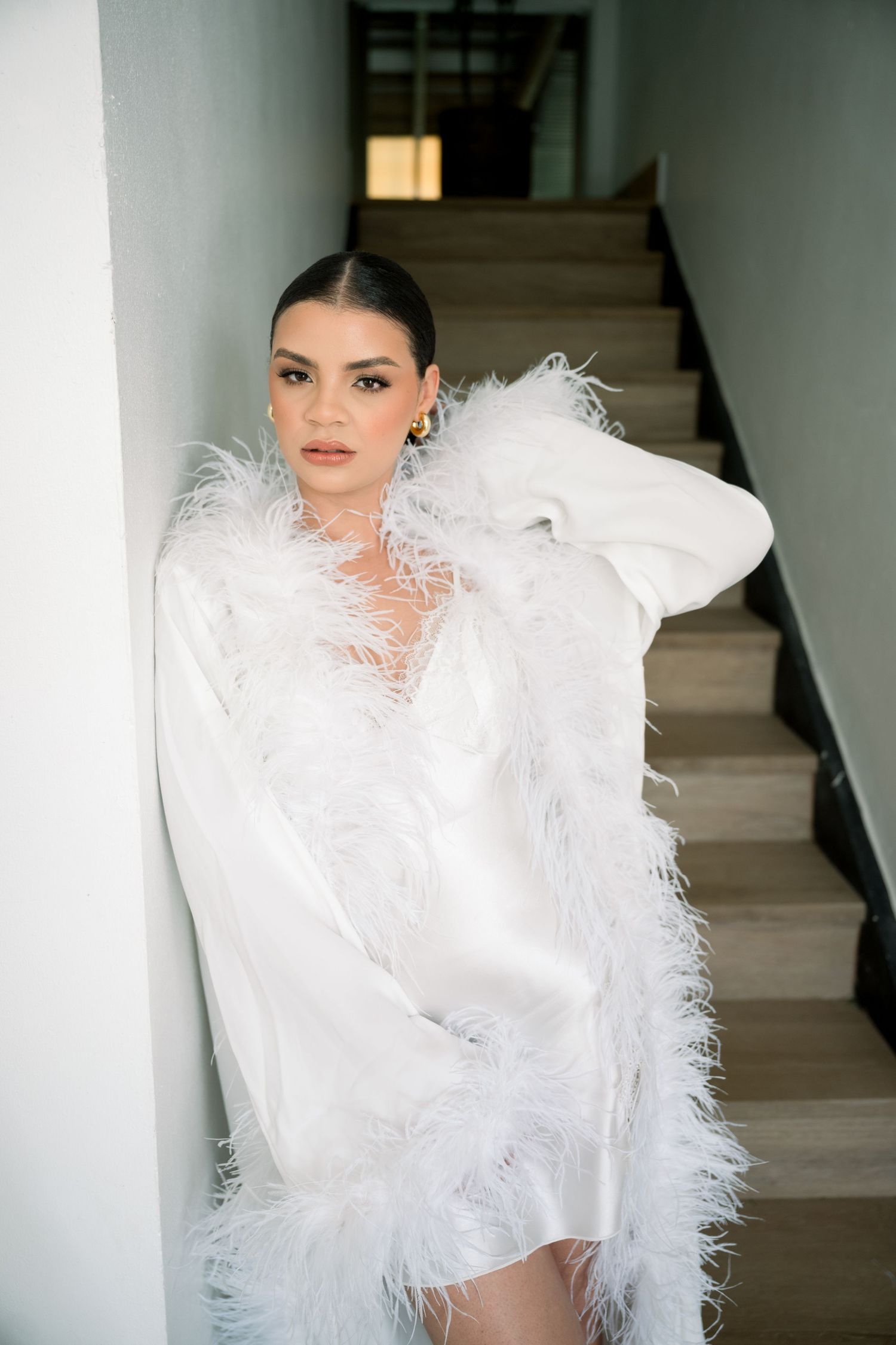A stunning white feathered wedding dress with dramatic details photographed on a staircase.