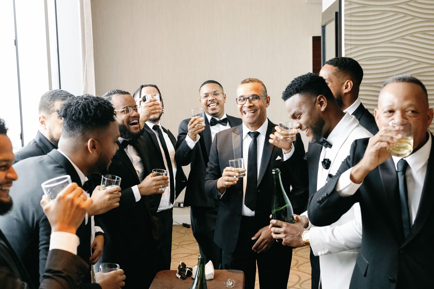 A celebratory gathering of people in formal black suits and tuxedos sharing drinks and laughter.