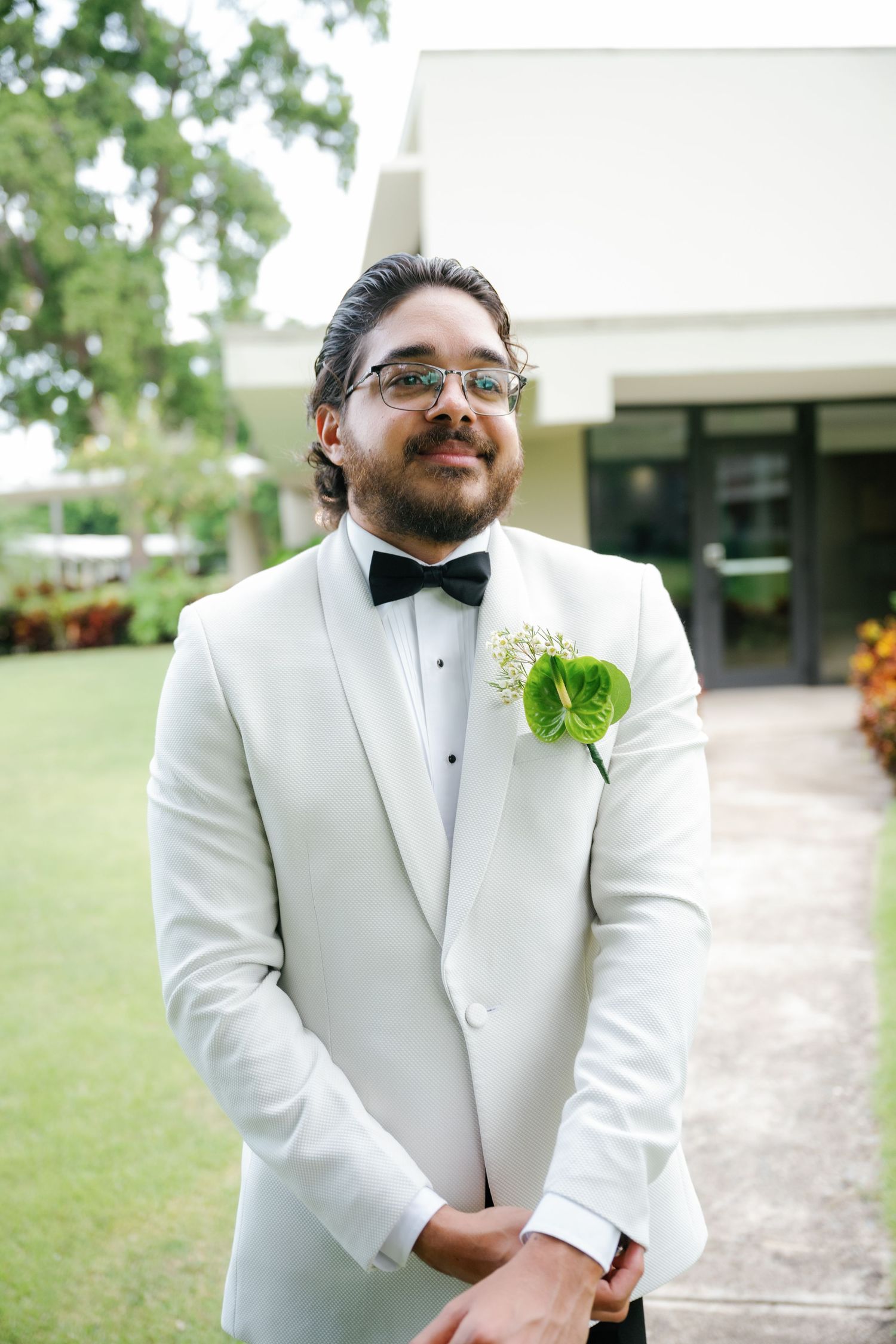 A formal event photo showing someone wearing a crisp white tuxedo with a green boutonniere.