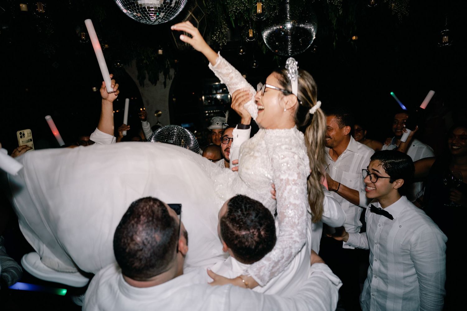 Chefs in white uniforms celebrating and raising their arms in a dimly lit restaurant space.