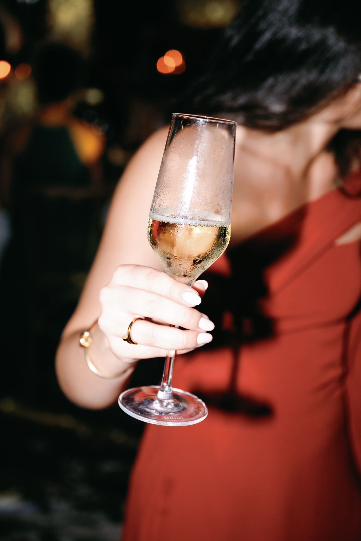 A hand holds a glass of sparkling wine against a dark background with bokeh lights.