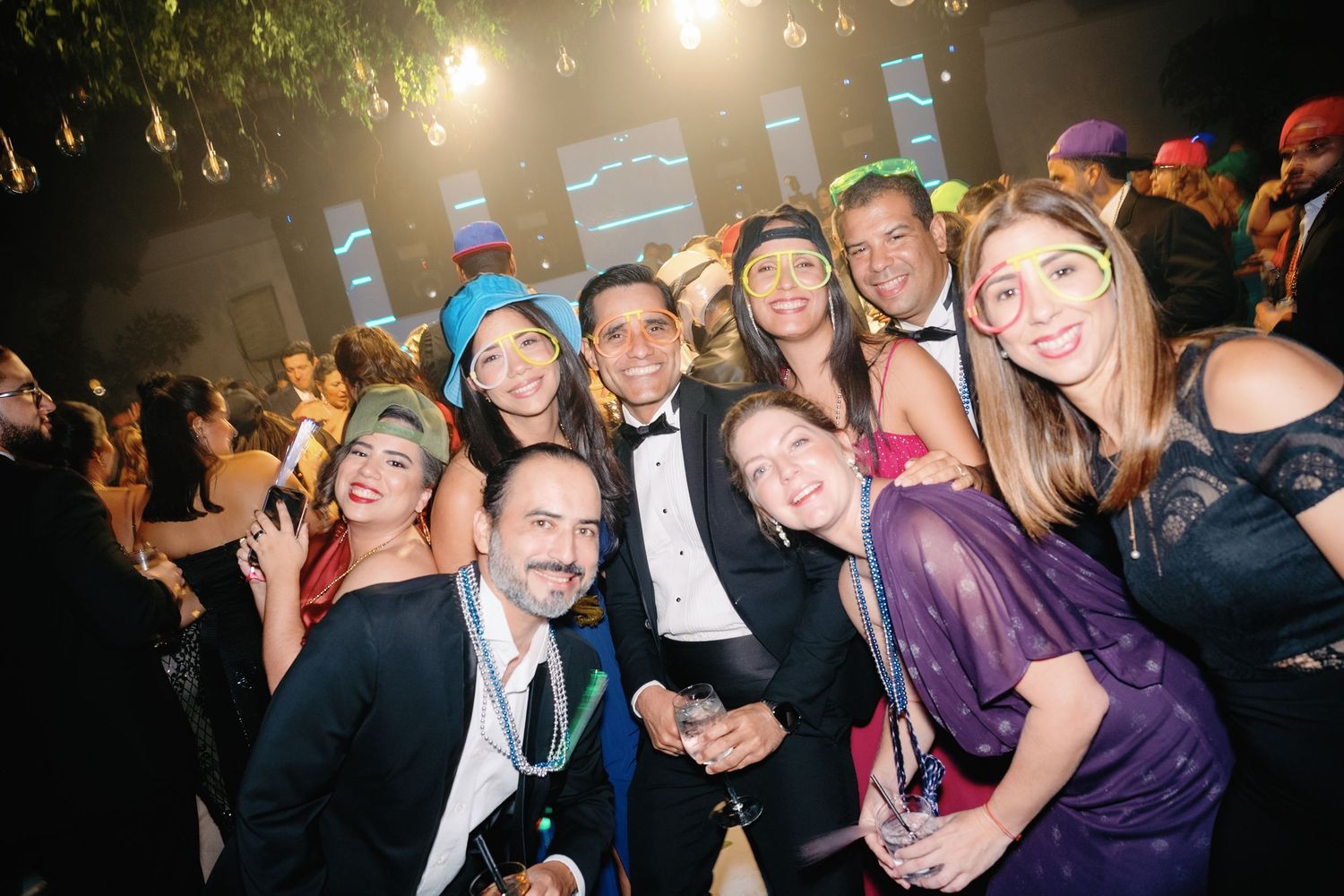 Crowd of people celebrating and dancing at a festive indoor party with colorful lighting.