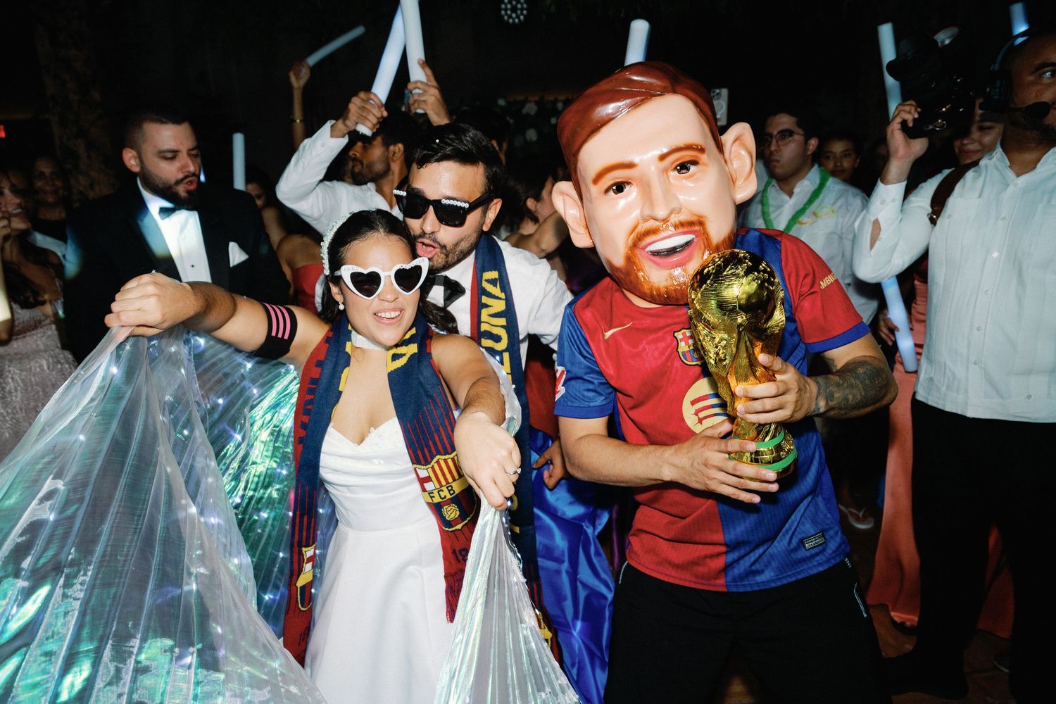 Wedding guests celebrate on dance floor wearing sports jerseys and formal attire at reception party.