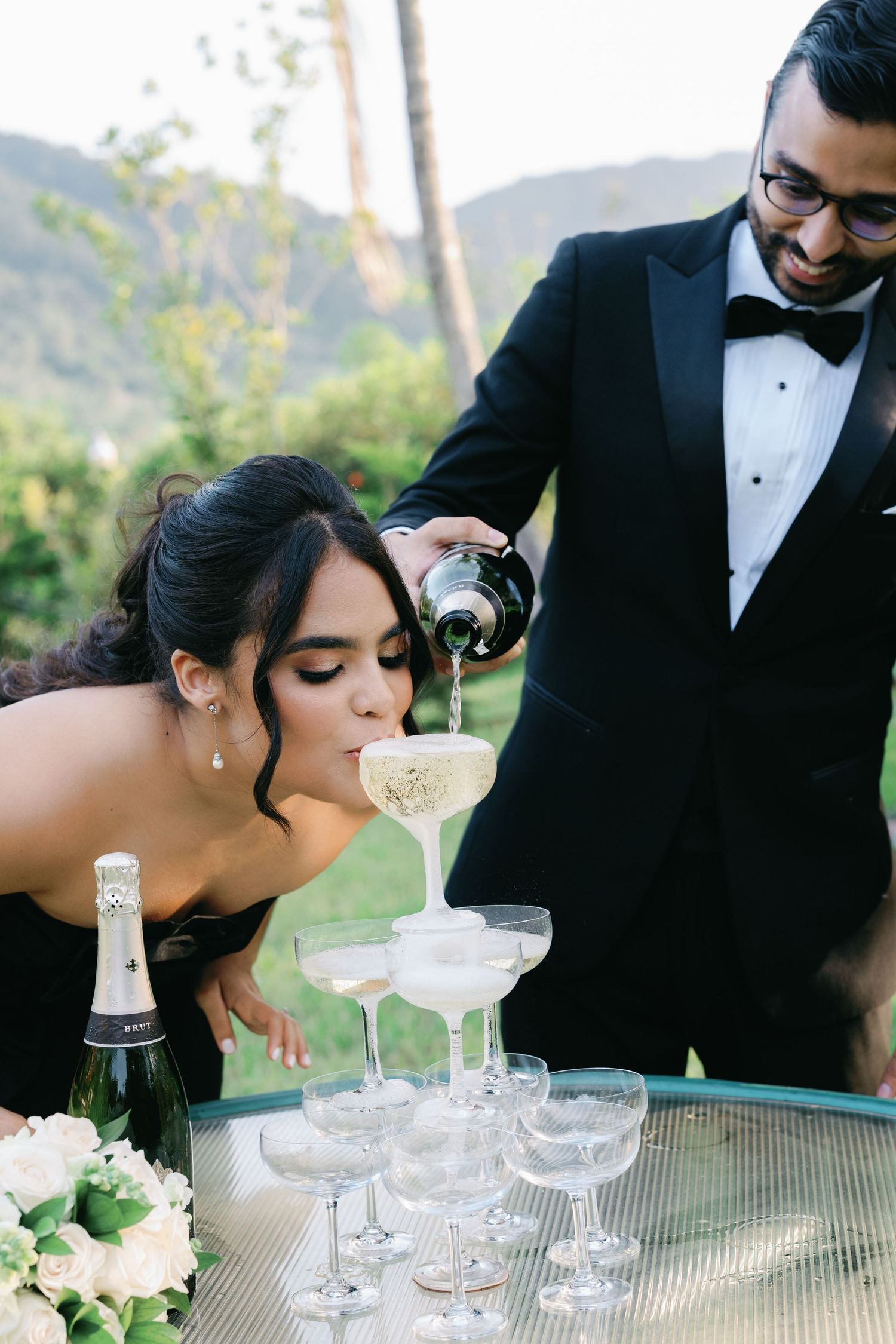 Champagne tower being poured at an elegant outdoor wedding reception.