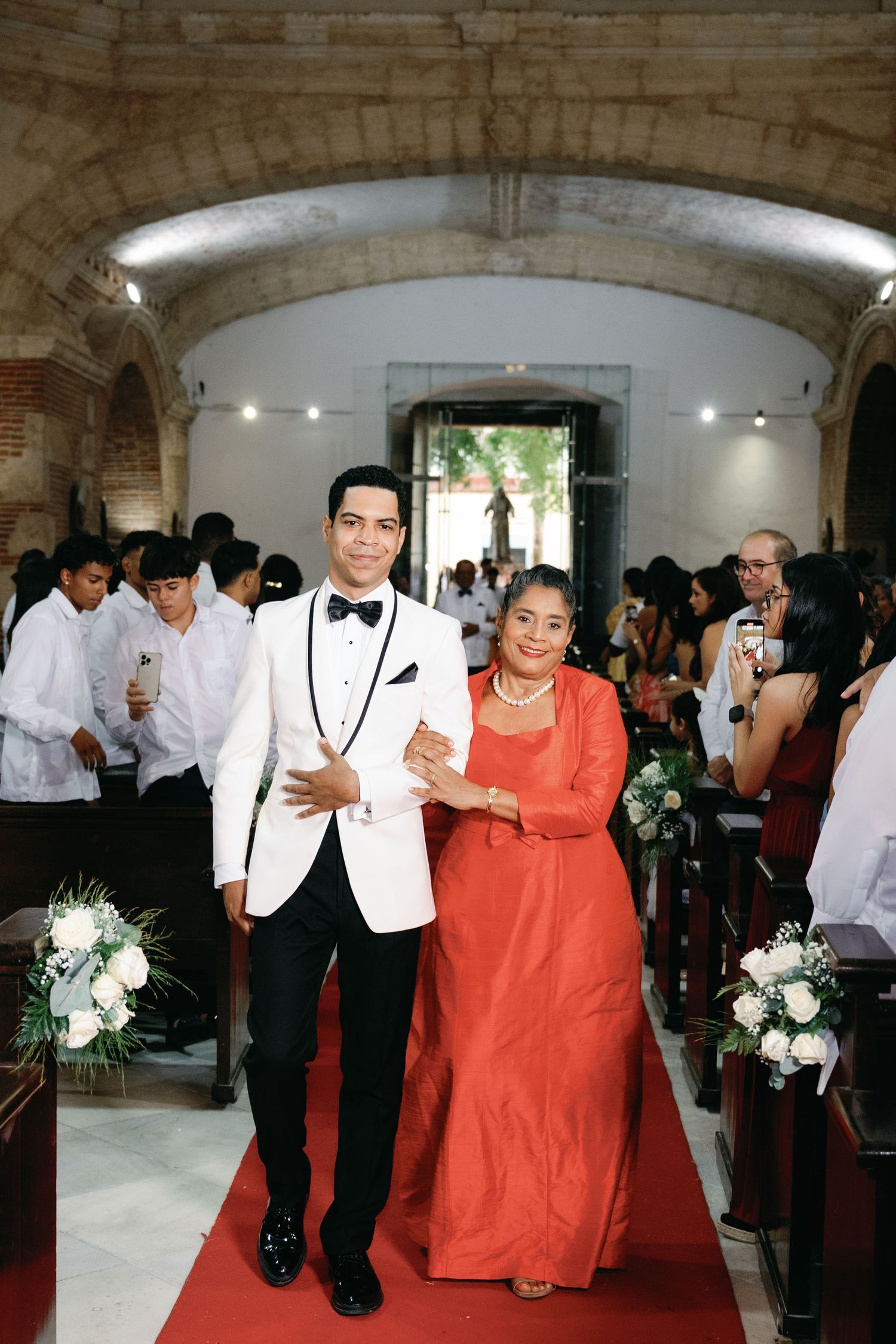 Wedding celebration in an elegant vaulted room with guests in formal attire and coral-colored accents.