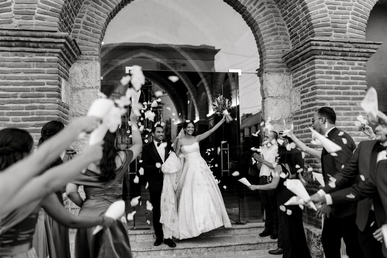 Wedding guests toss rice and confetti at newlyweds outside a brick church building in a joyful celebration sequence.